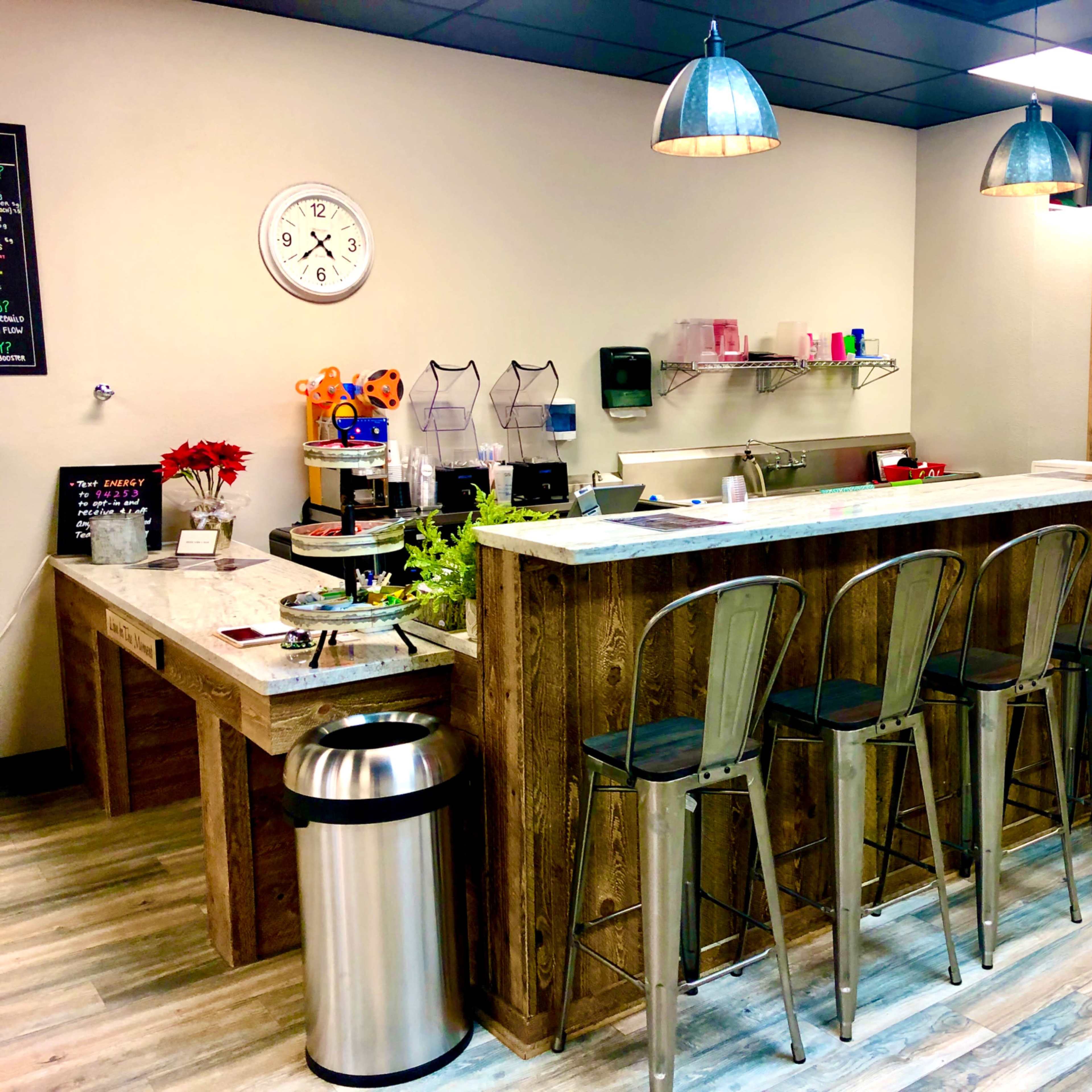 A modern café interior featuring a wooden counter with high stools, a clock on the wall, and various kitchen items arranged on the counter.