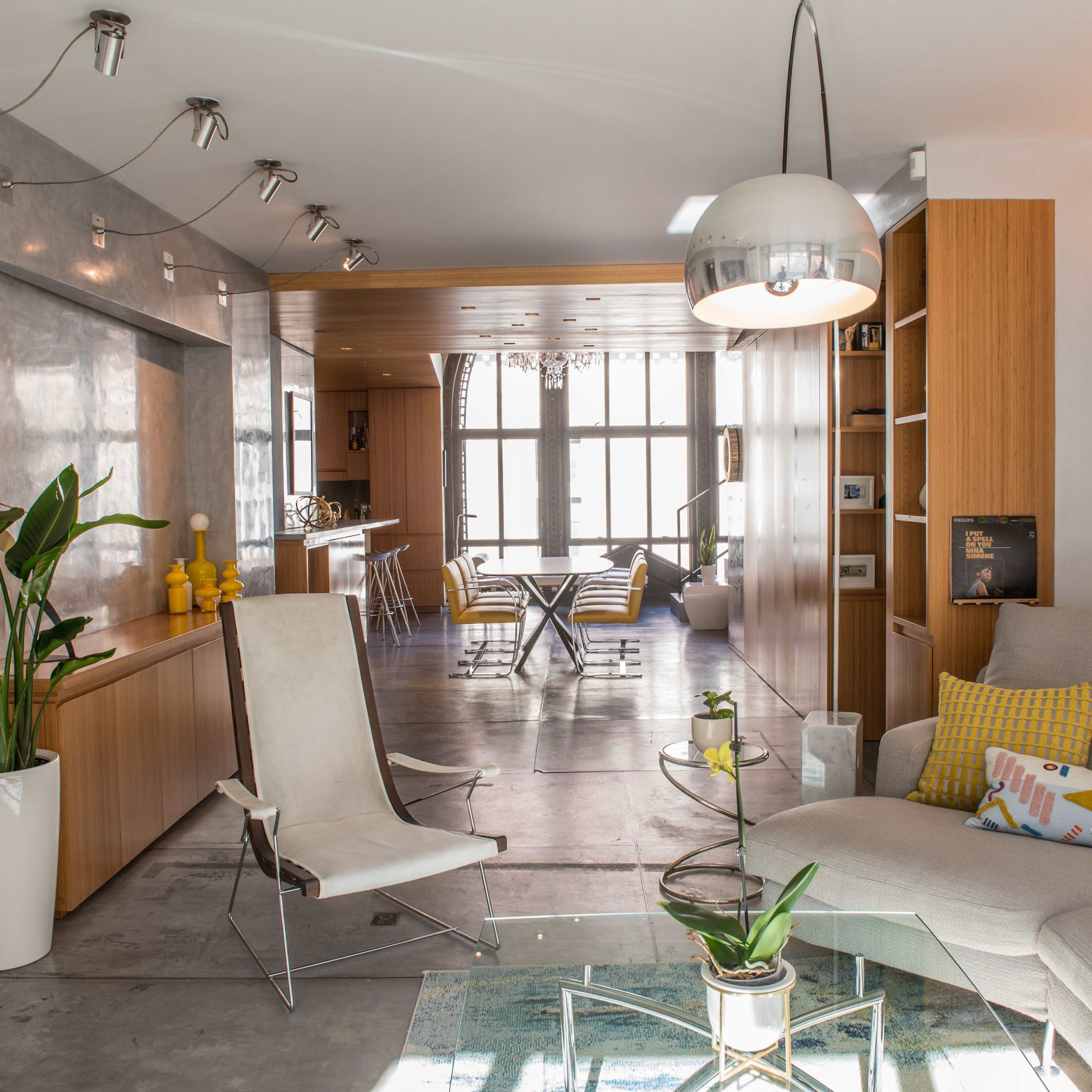 A contemporary living space featuring a light-colored sectional sofa, a glass coffee table, and an open layout that connects to a dining area with modern furnishings.