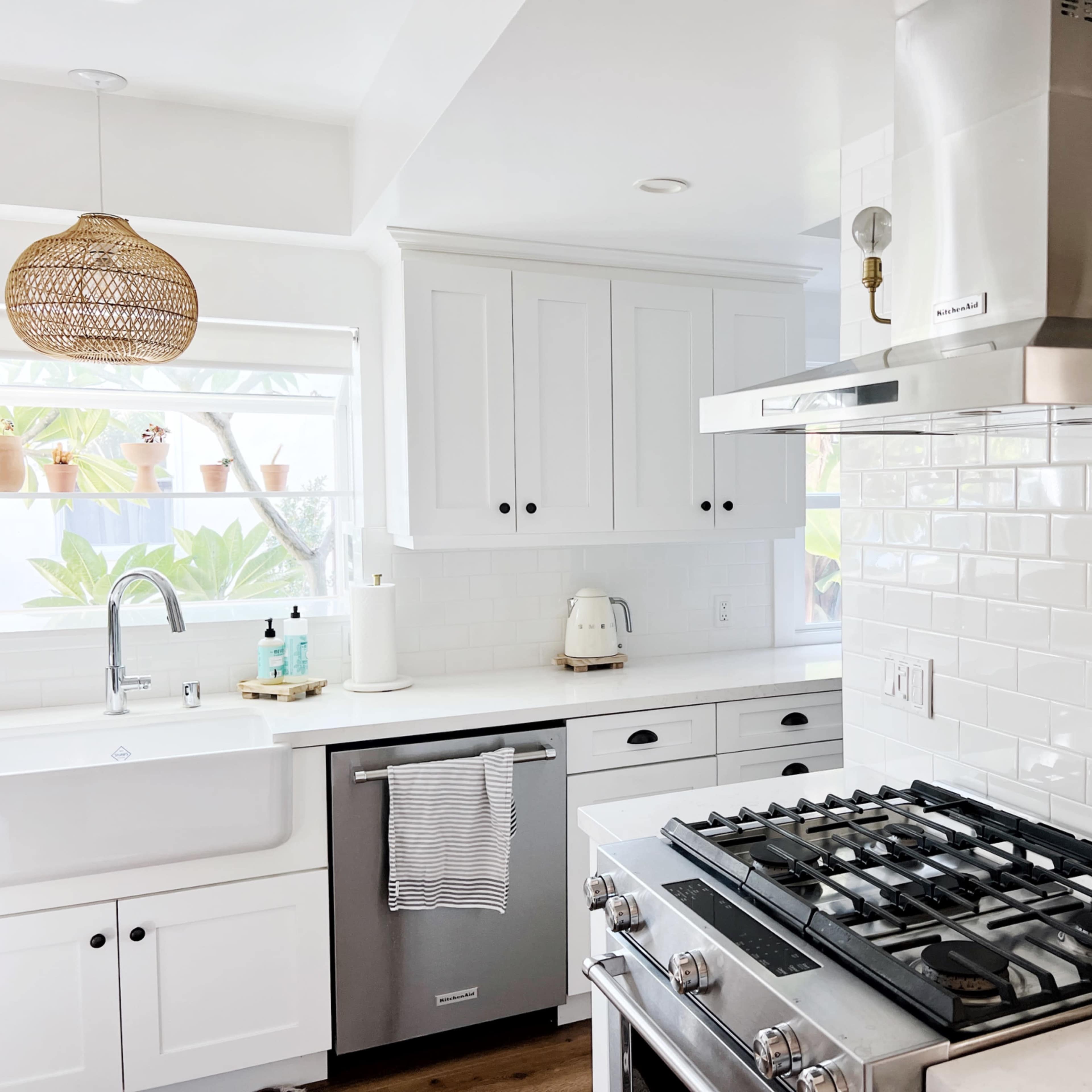 A modern kitchen features white cabinets, a stainless steel range hood, and a gas stove with a visible pot rack.