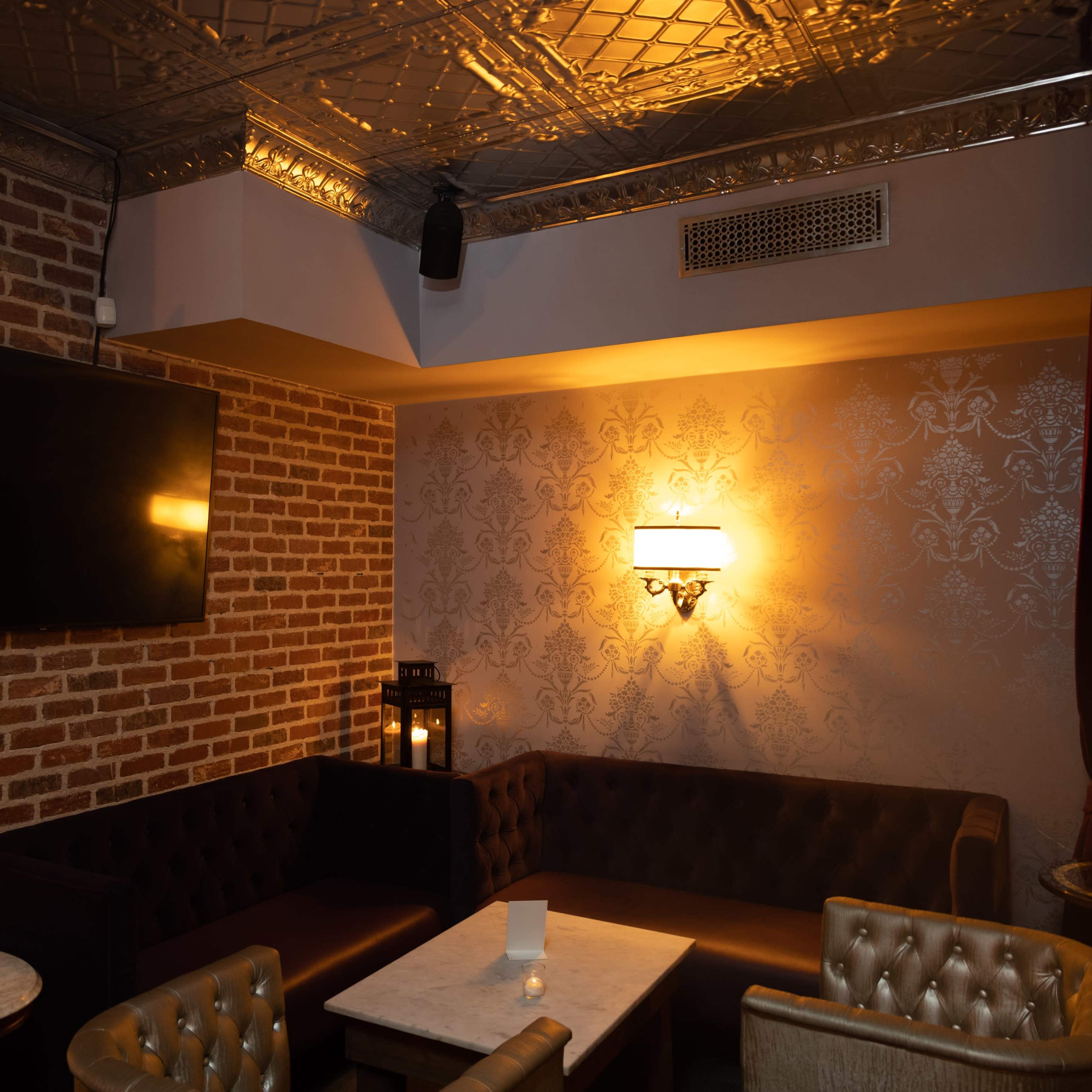 A cozy lounge area with plush seating, a marble table, and soft lighting against a brick wall.