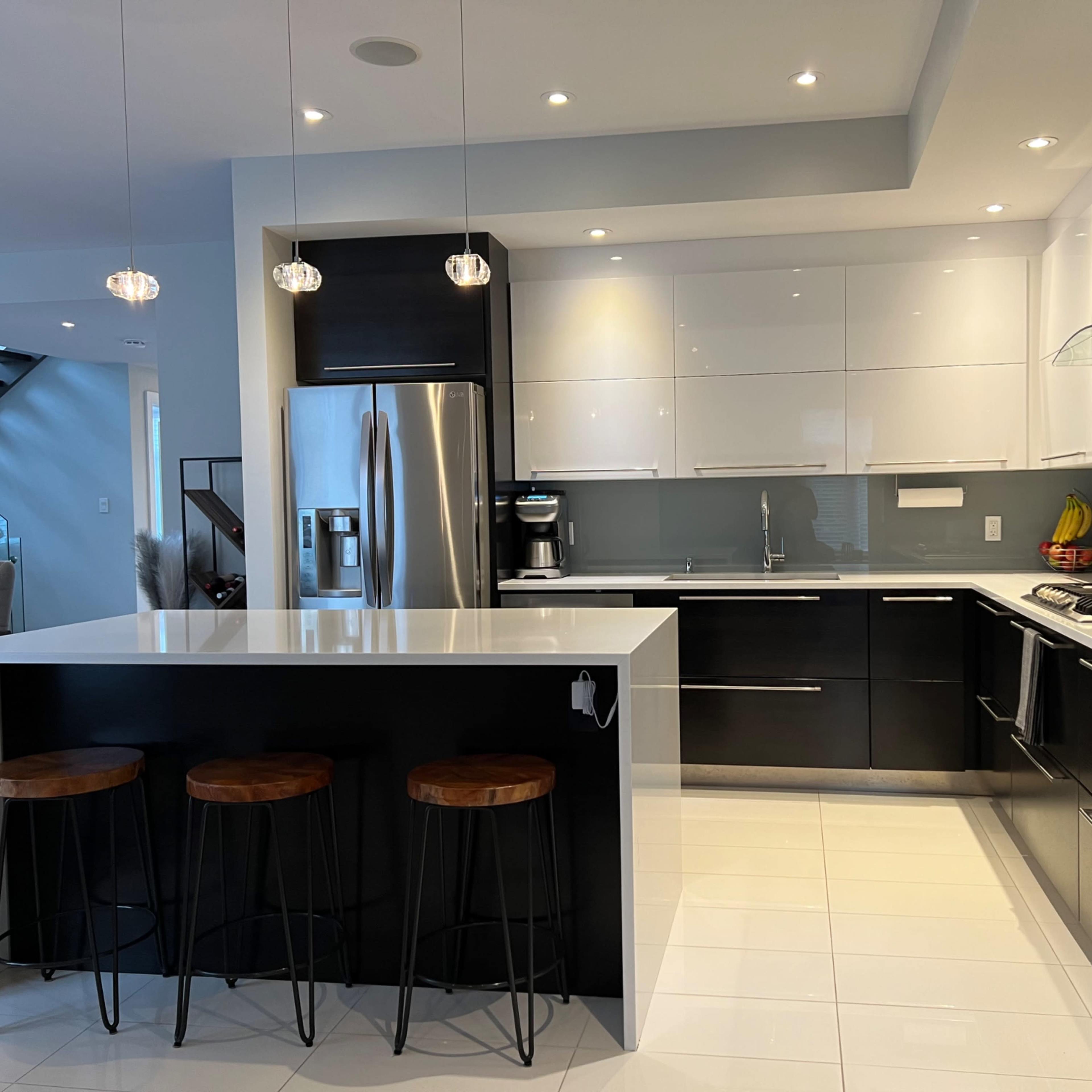 A modern kitchen featuring sleek black and white cabinetry, stainless steel appliances, and three bar stools at a white island counter.