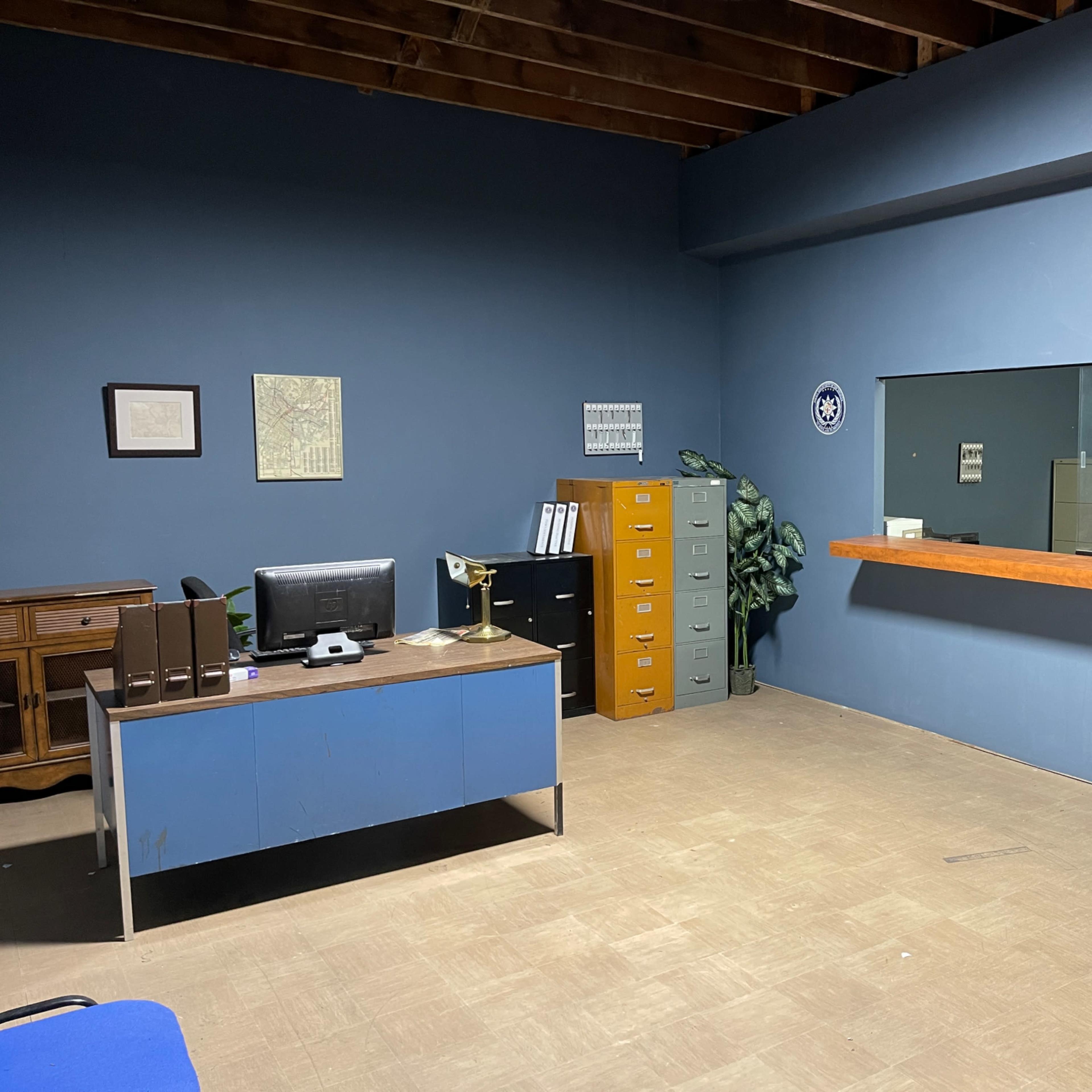 An office with a blue wall, a desk with a computer, a filing cabinet, and a large window counter.