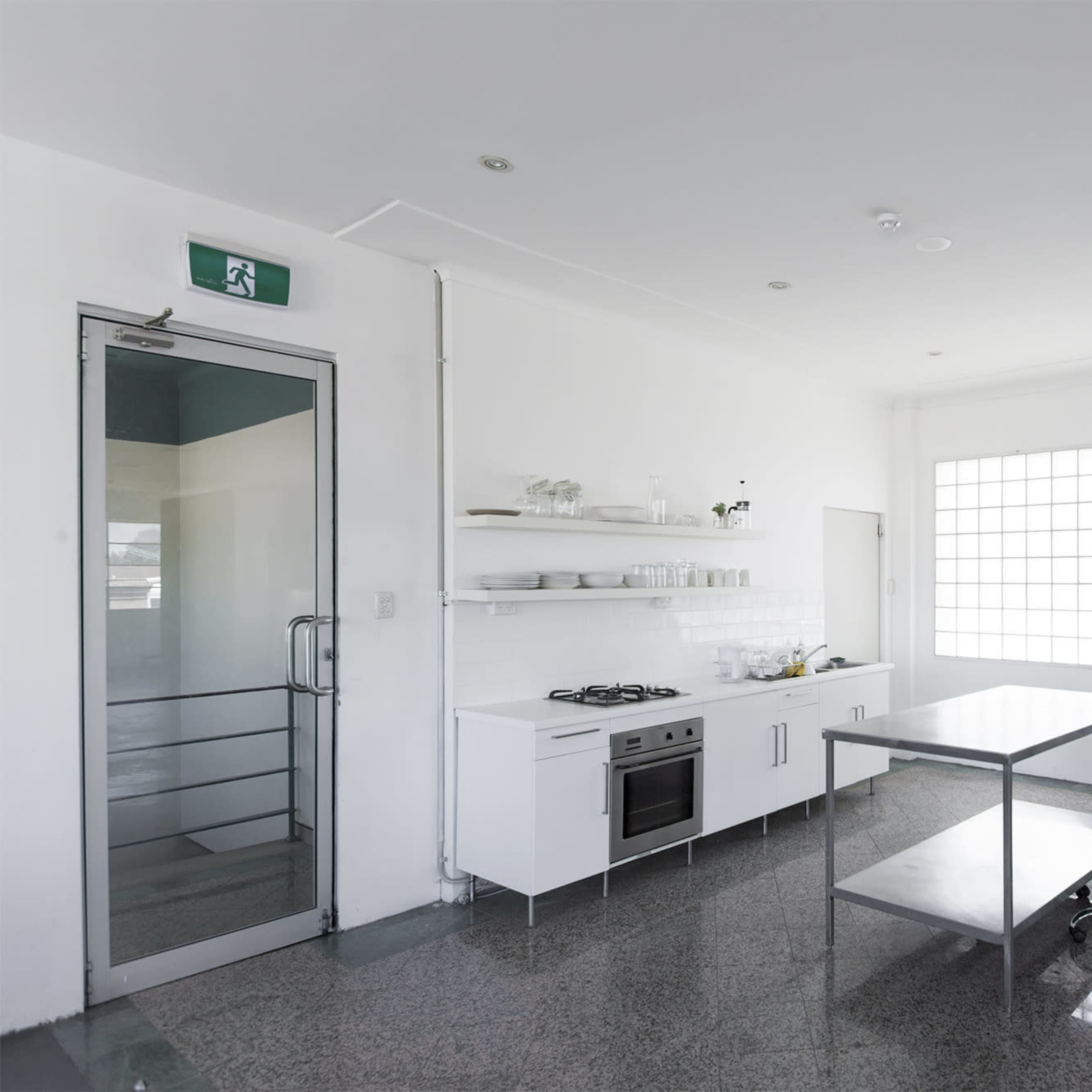 A modern kitchen features white cabinetry, a metal dining table, and large windows allowing ample natural light.