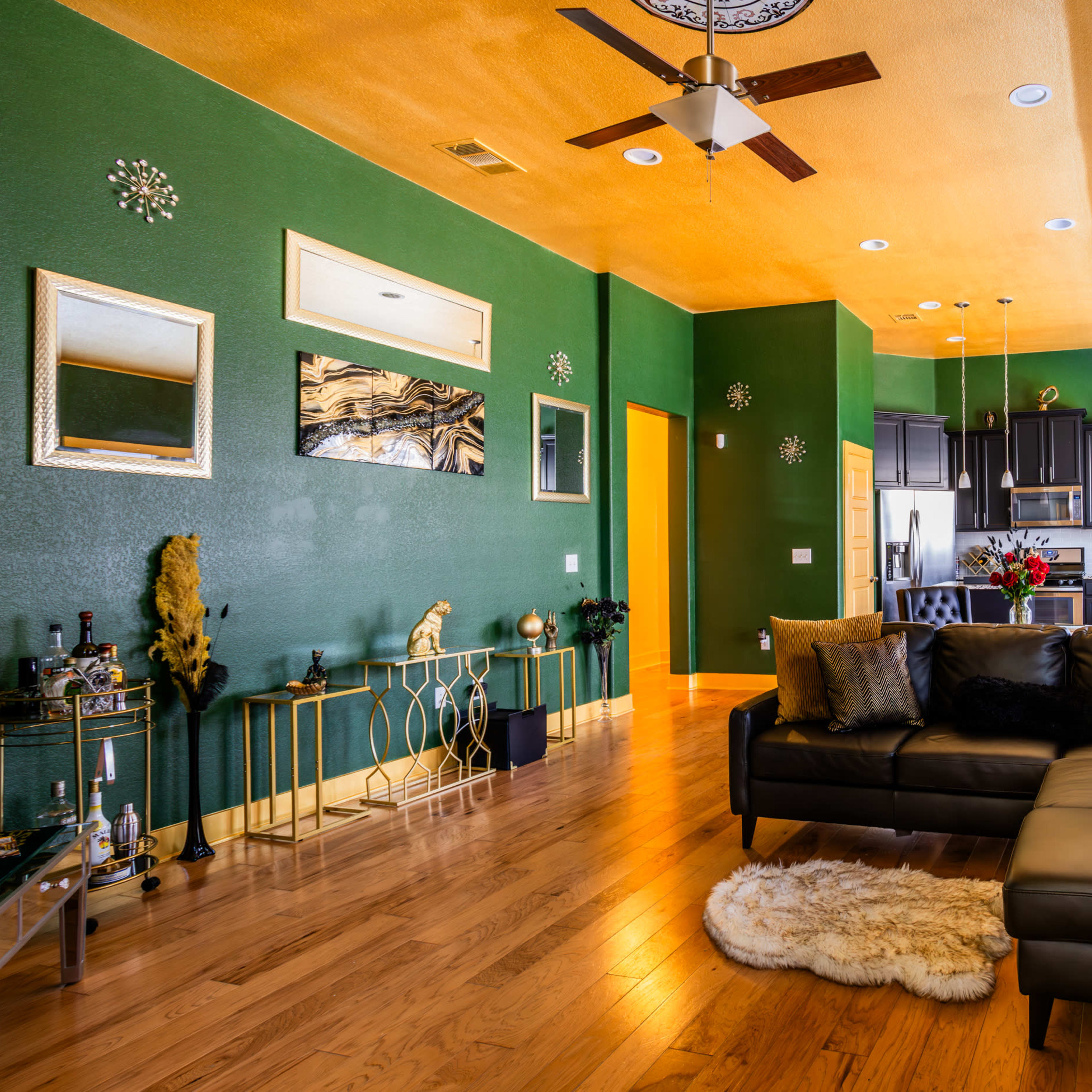 A modern living room with green walls, wooden flooring, and a dark sectional sofa, featuring decorative elements and plants.