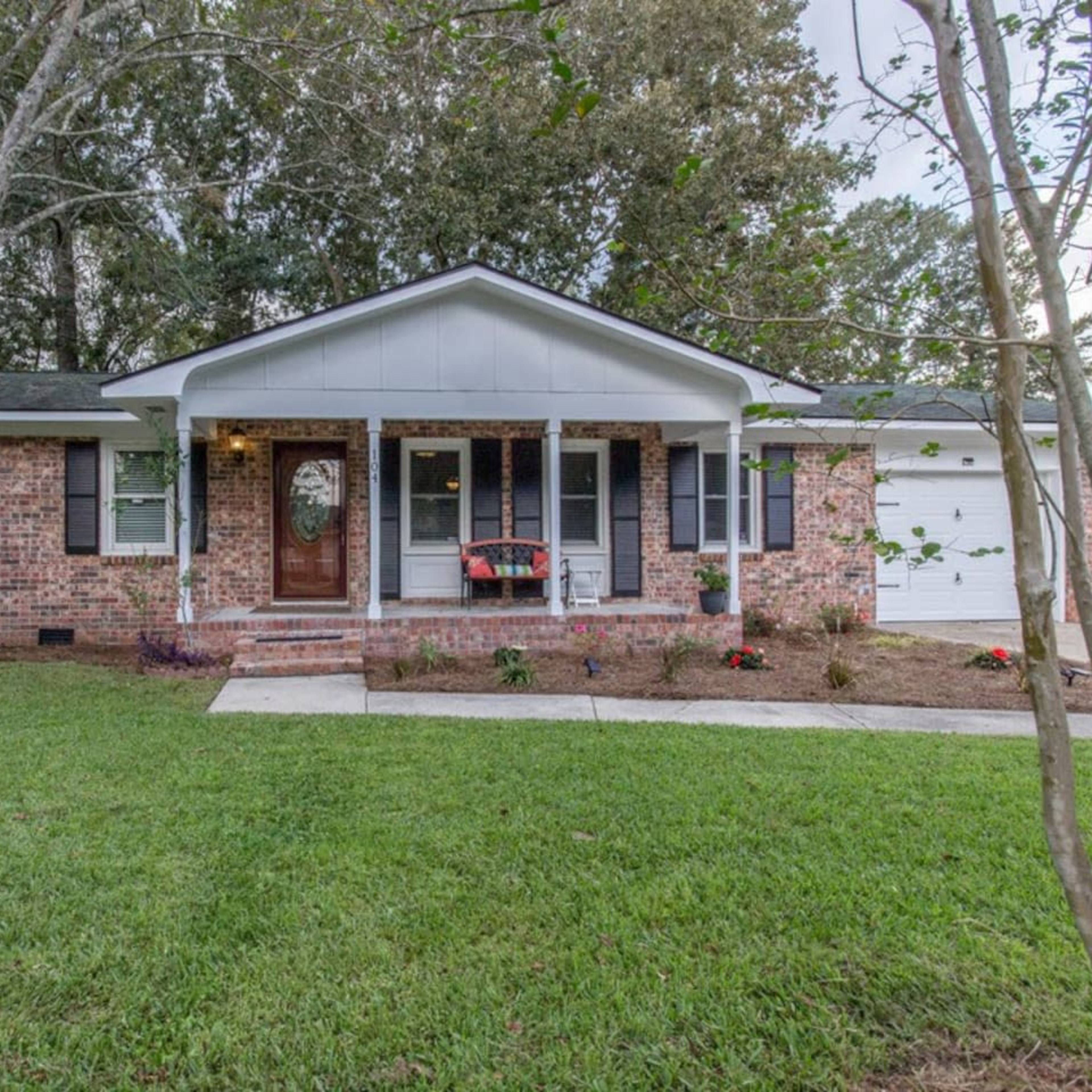 A brick house with a white roof and porch is surrounded by a green lawn and trees.