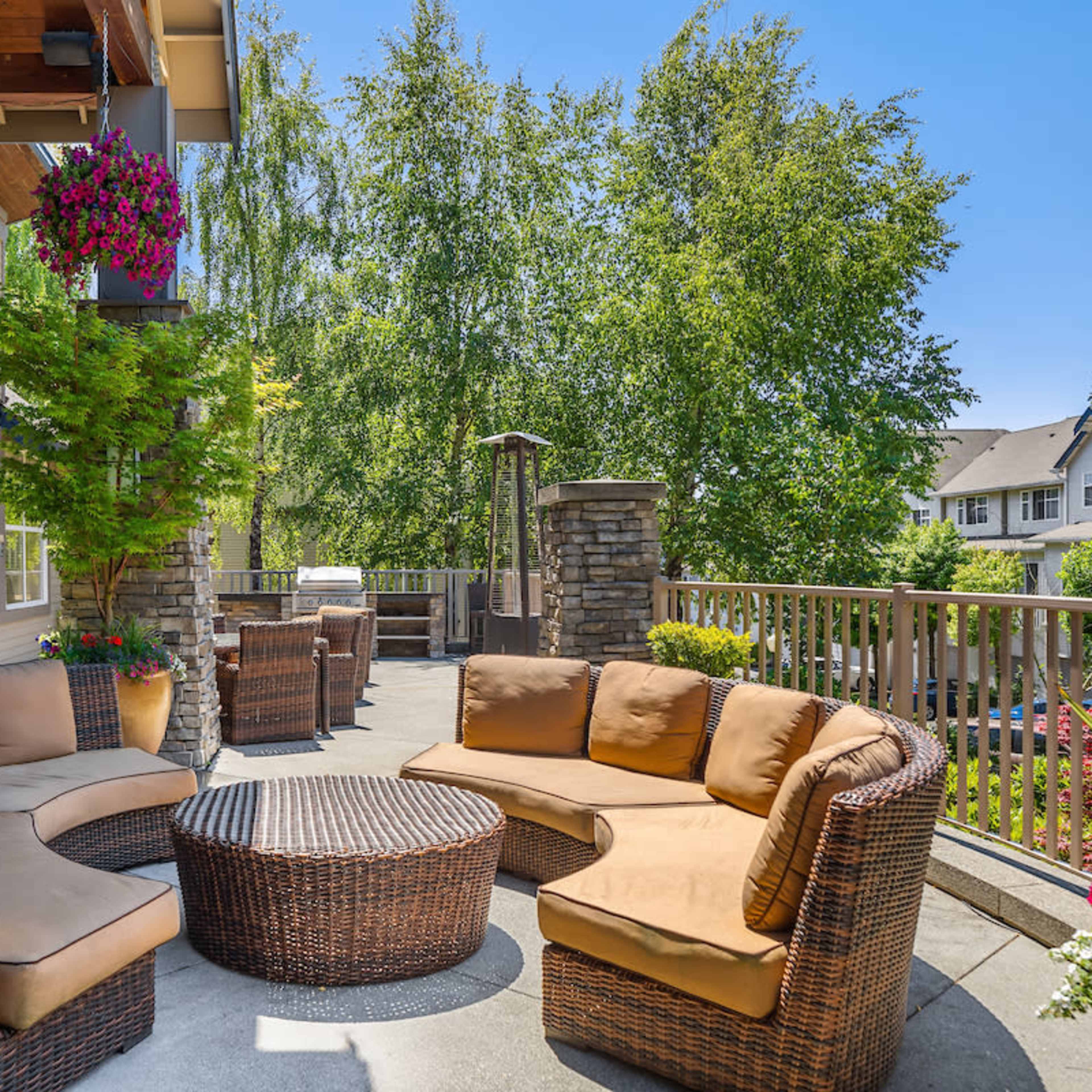 A patio area with a circular wicker seating arrangement and a central coffee table, surrounded by greenery and residential buildings in the background.