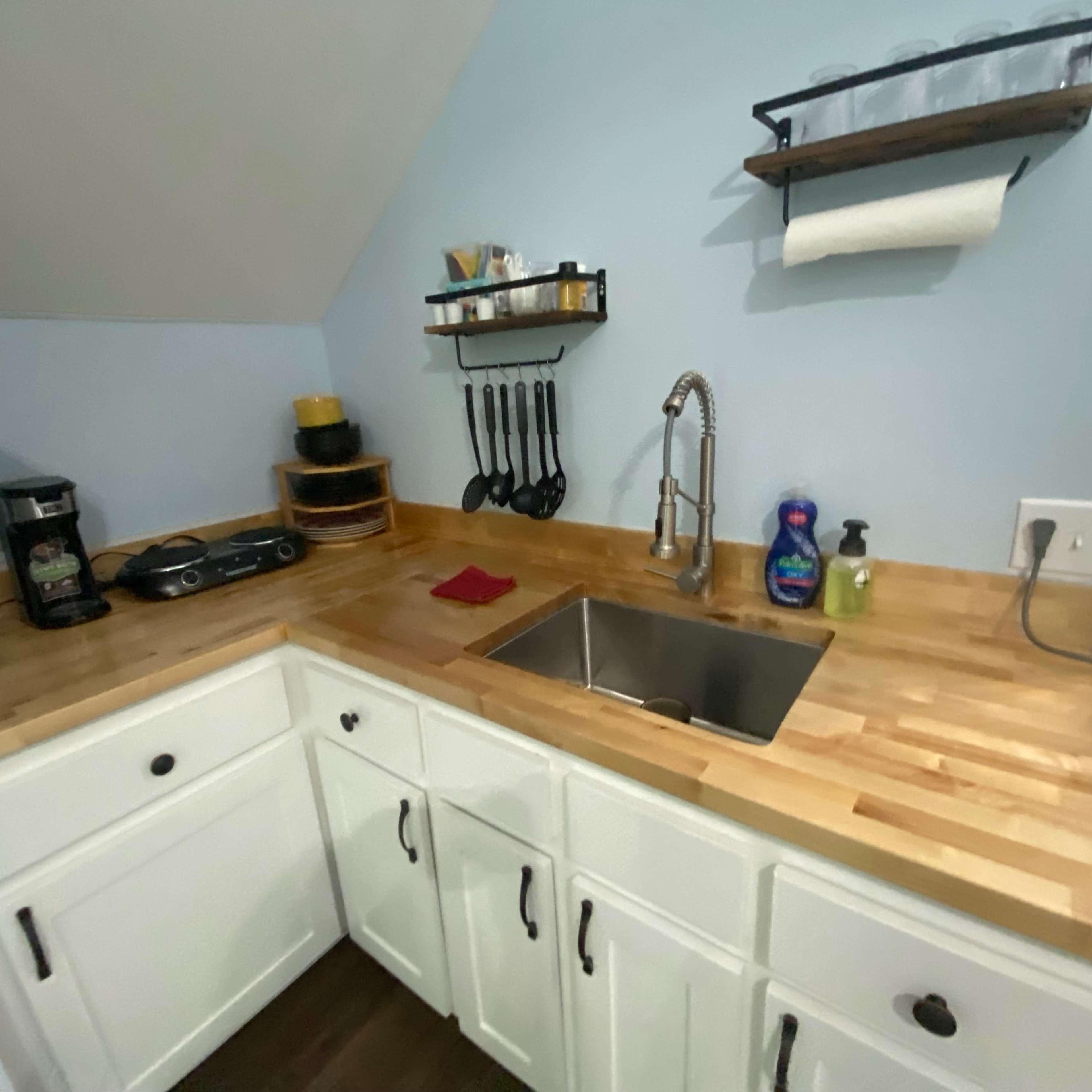 A compact kitchen corner with a stainless steel sink, wooden countertops, and organized utensils on a wall-mounted shelf.