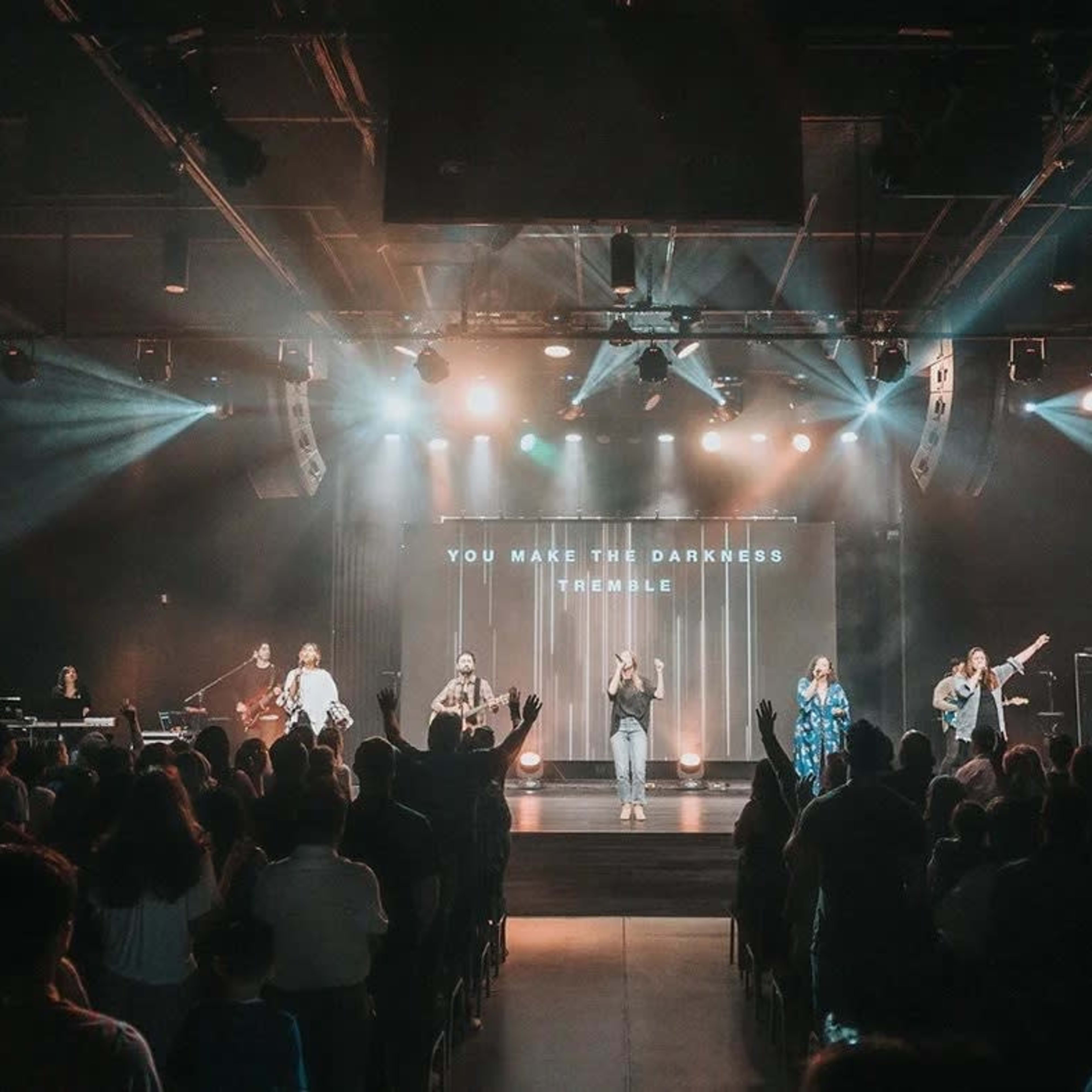 A group of musicians performs on stage in front of an audience in a well-lit auditorium.