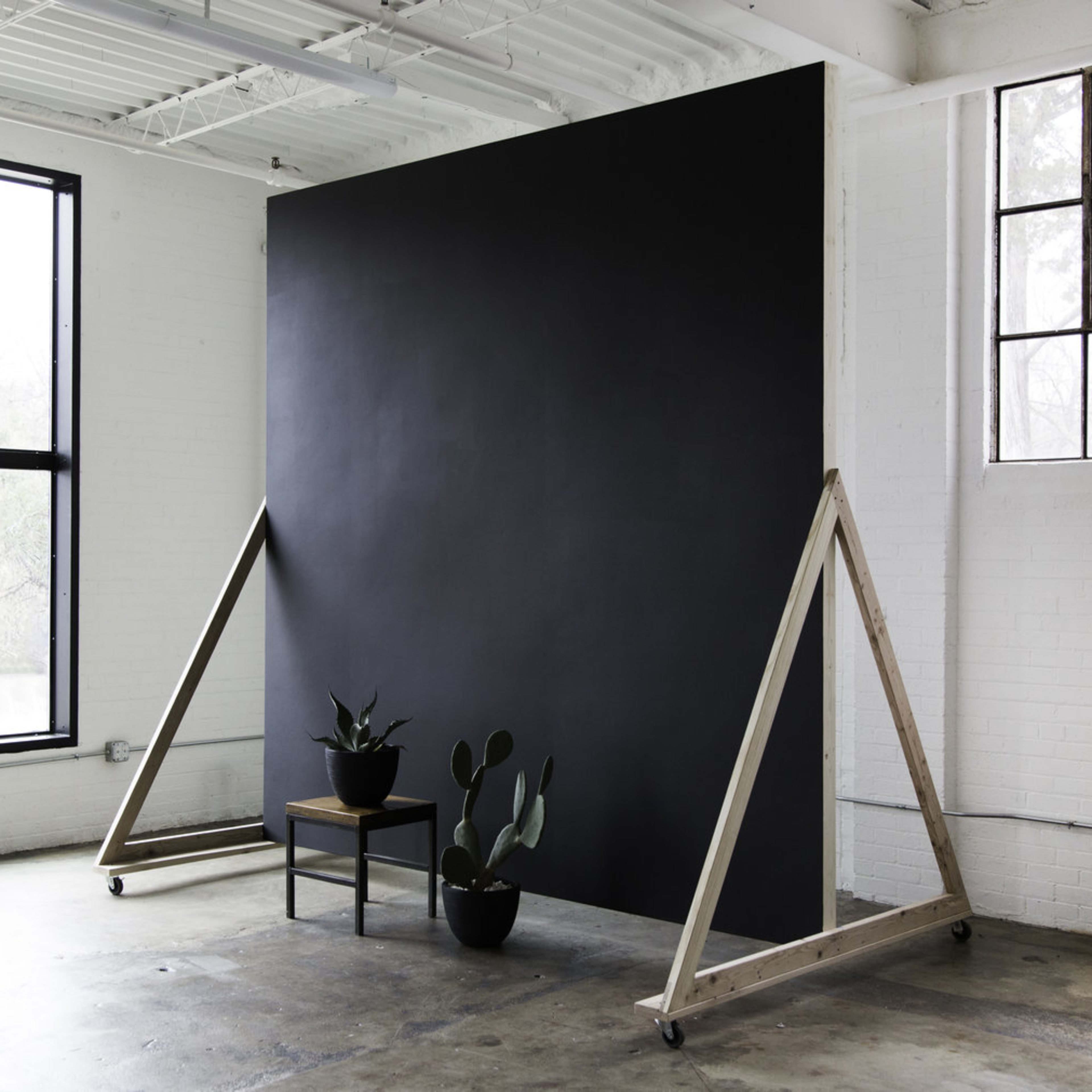 A minimalist interior space featuring a large black backdrop, a wooden chair, and two potted plants.
