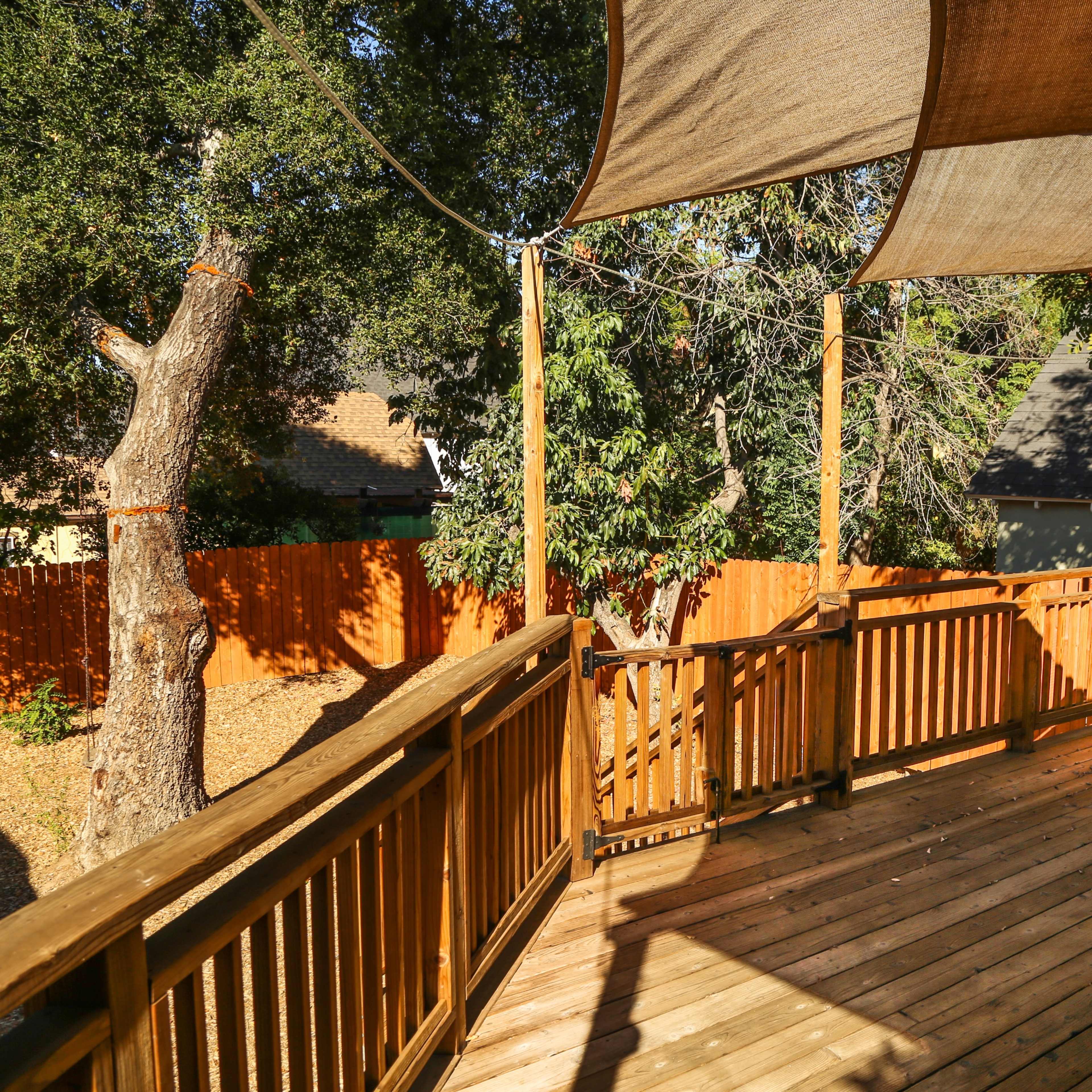 A wooden deck with a shaded area, surrounded by trees and a wooden fence.