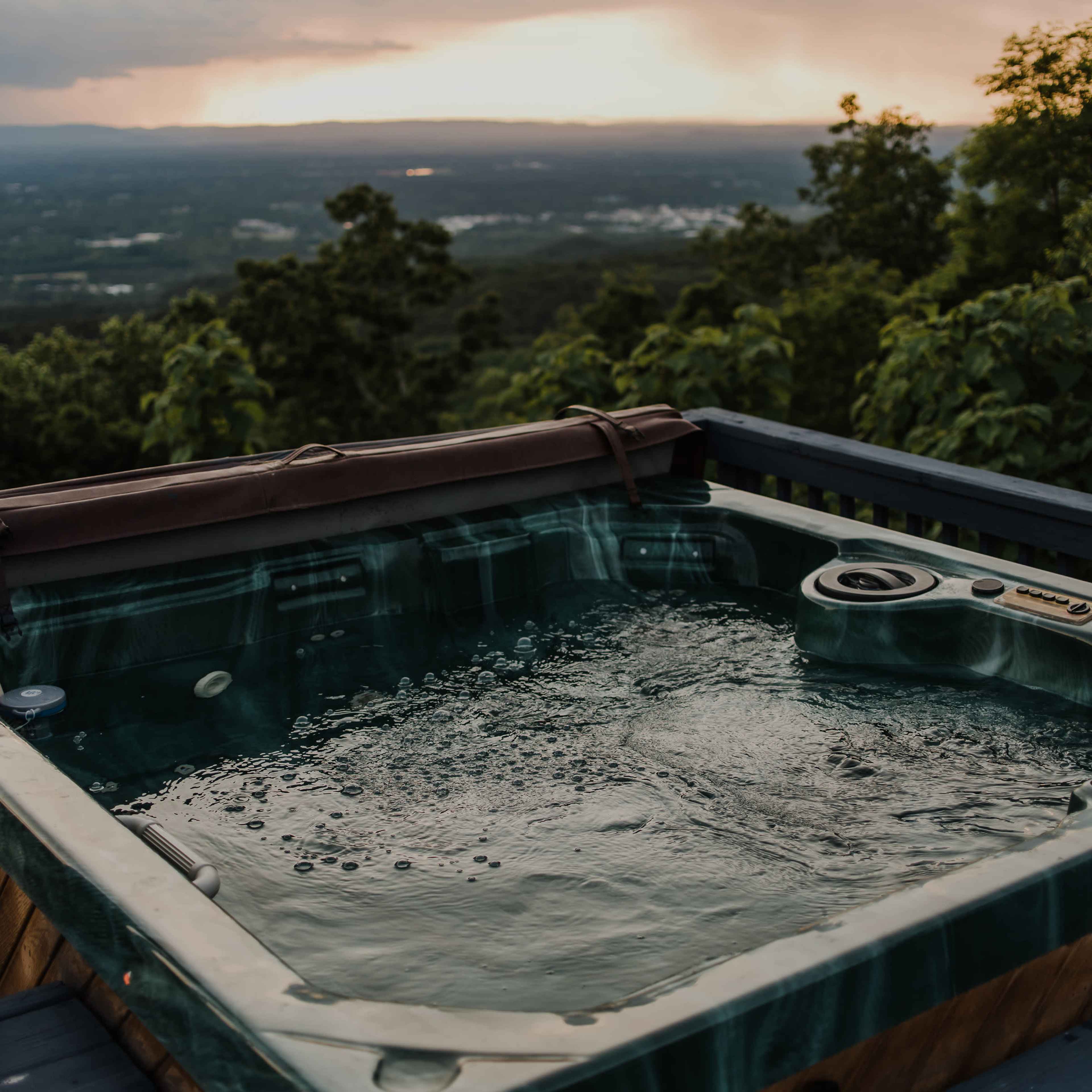 A hot tub filled with bubbling water overlooks a valley and distant mountains under a cloudy sky.