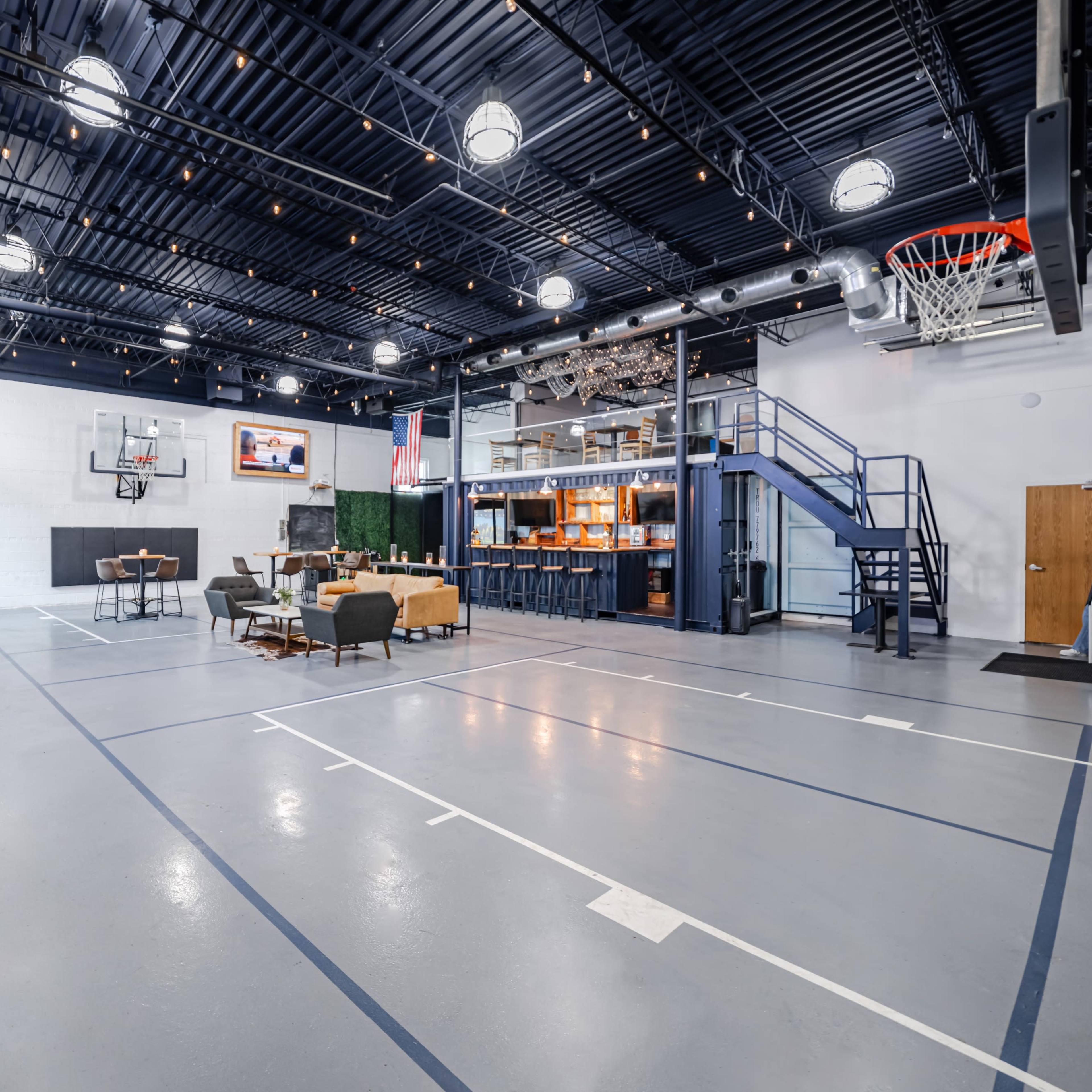 A spacious indoor basketball court with seating areas, a television, and a bar in a recreational setting.