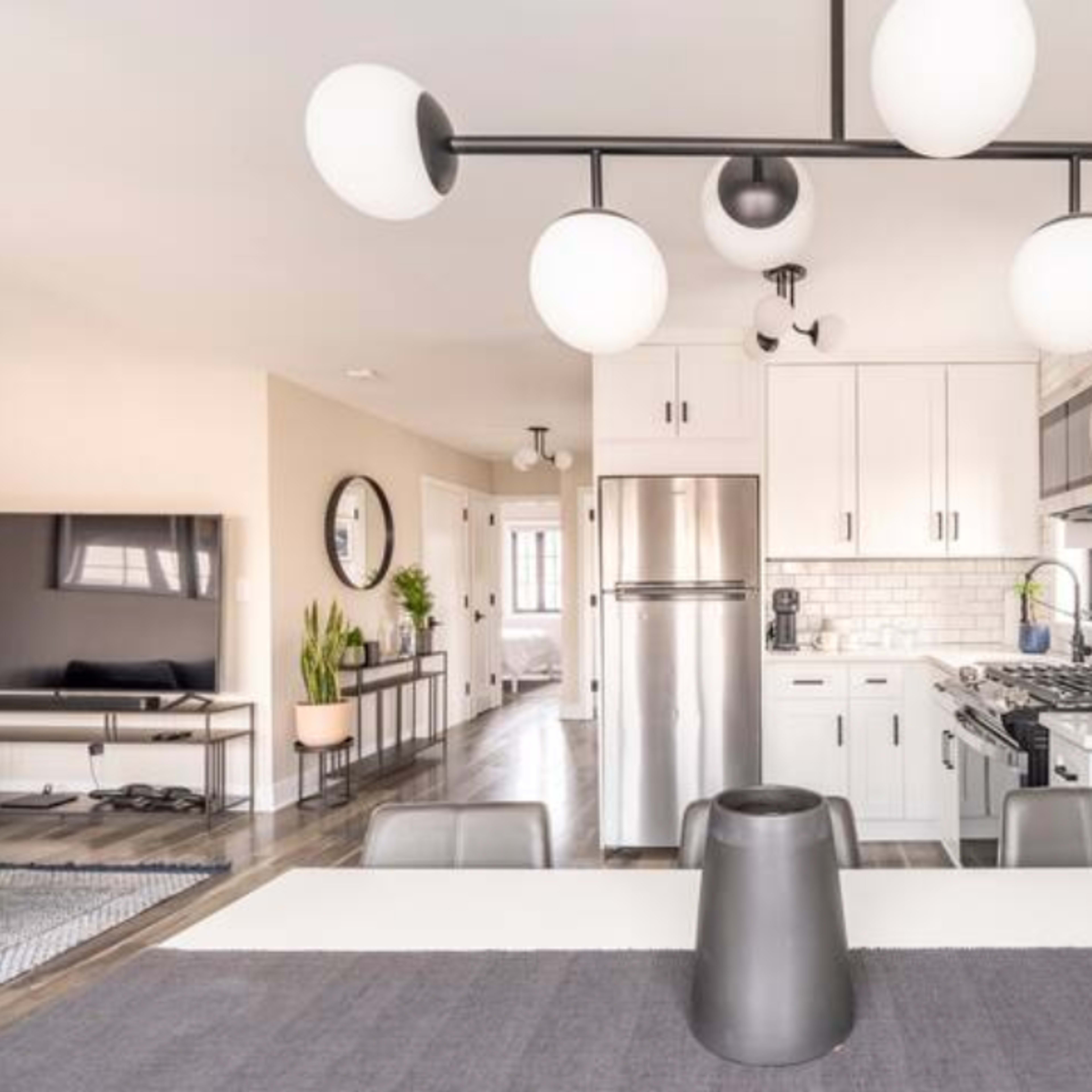 A modern kitchen and dining area featuring a sleek table with a gray runner, a contemporary light fixture, and stainless steel appliances.