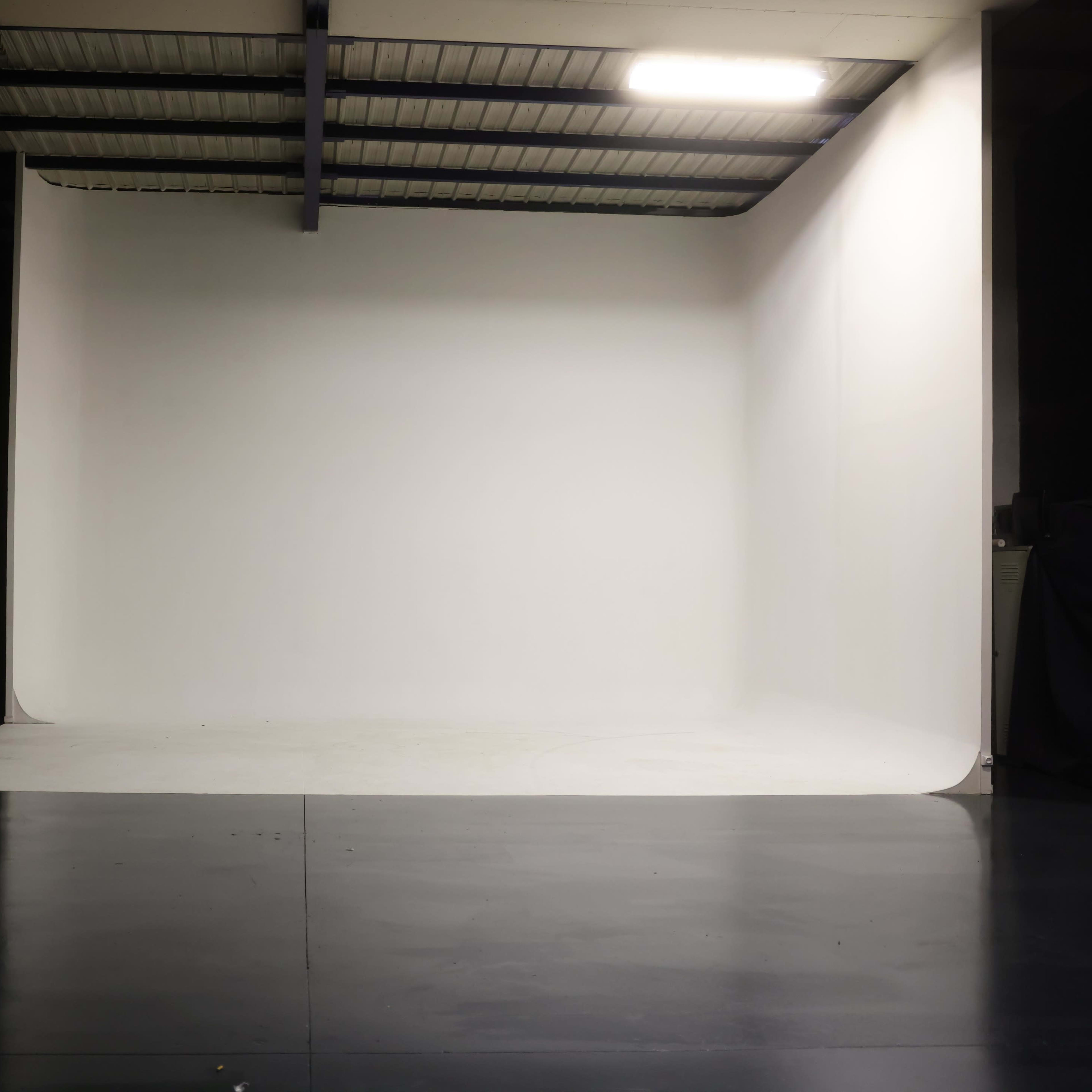 A spacious photography studio with a large seamless white backdrop and a polished dark floor.
