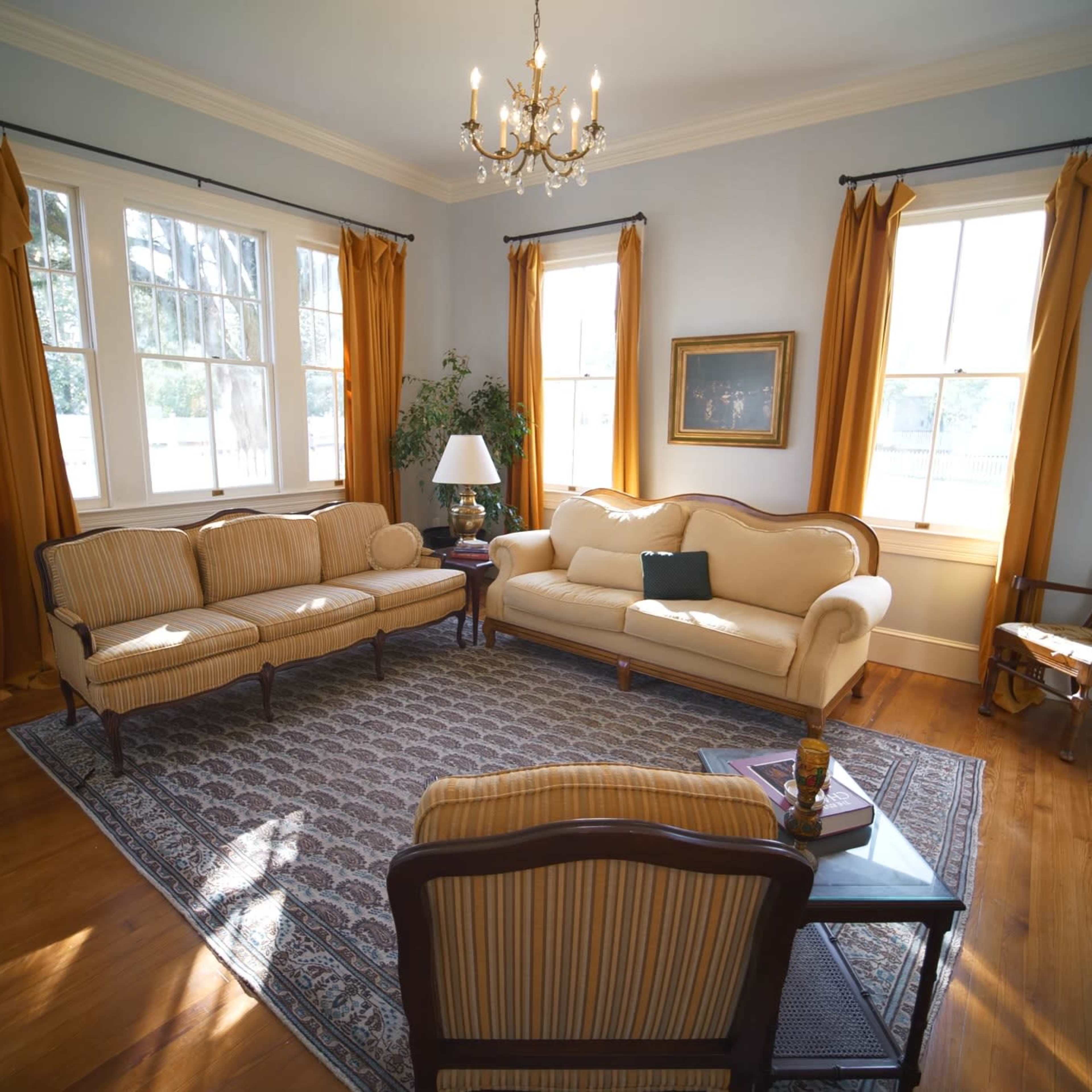 A living room featuring a beige couch and loveseat, a wooden coffee table, and large windows with yellow curtains.