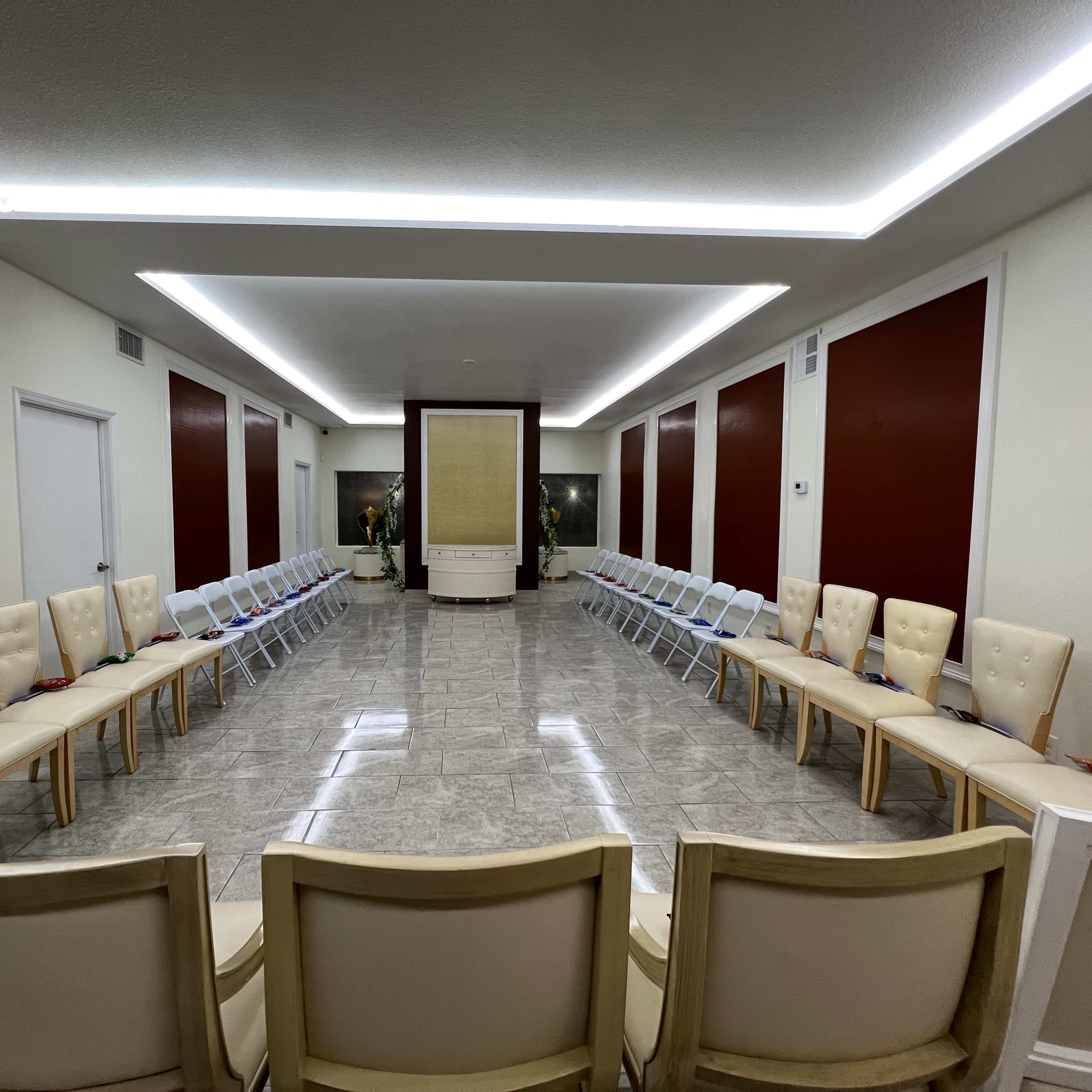 A spacious room arranged with two rows of beige chairs facing each other, centered around a decorative element on the back wall.