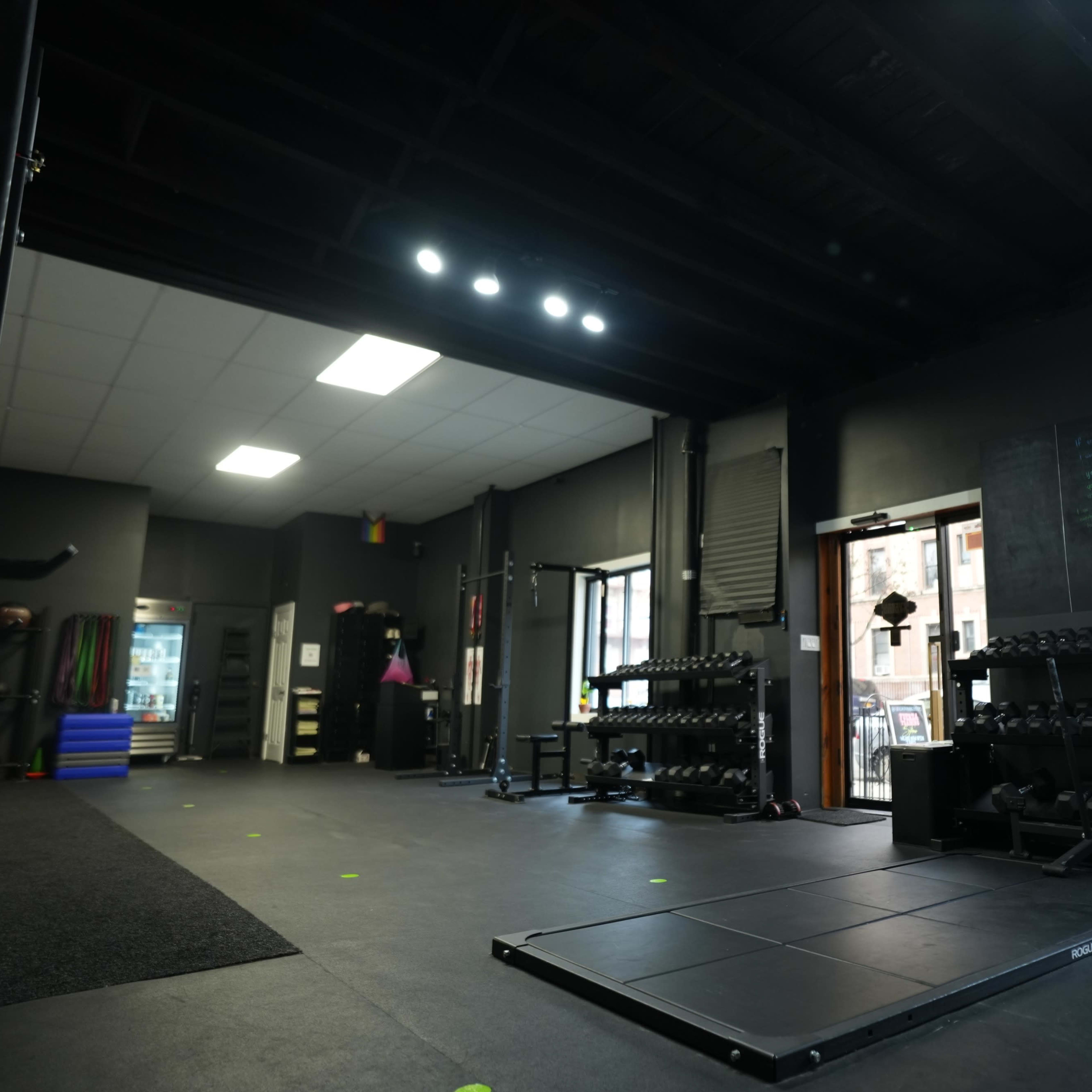 A gym interior featuring weightlifting equipment, a designated lifting platform, and large windows letting in natural light.