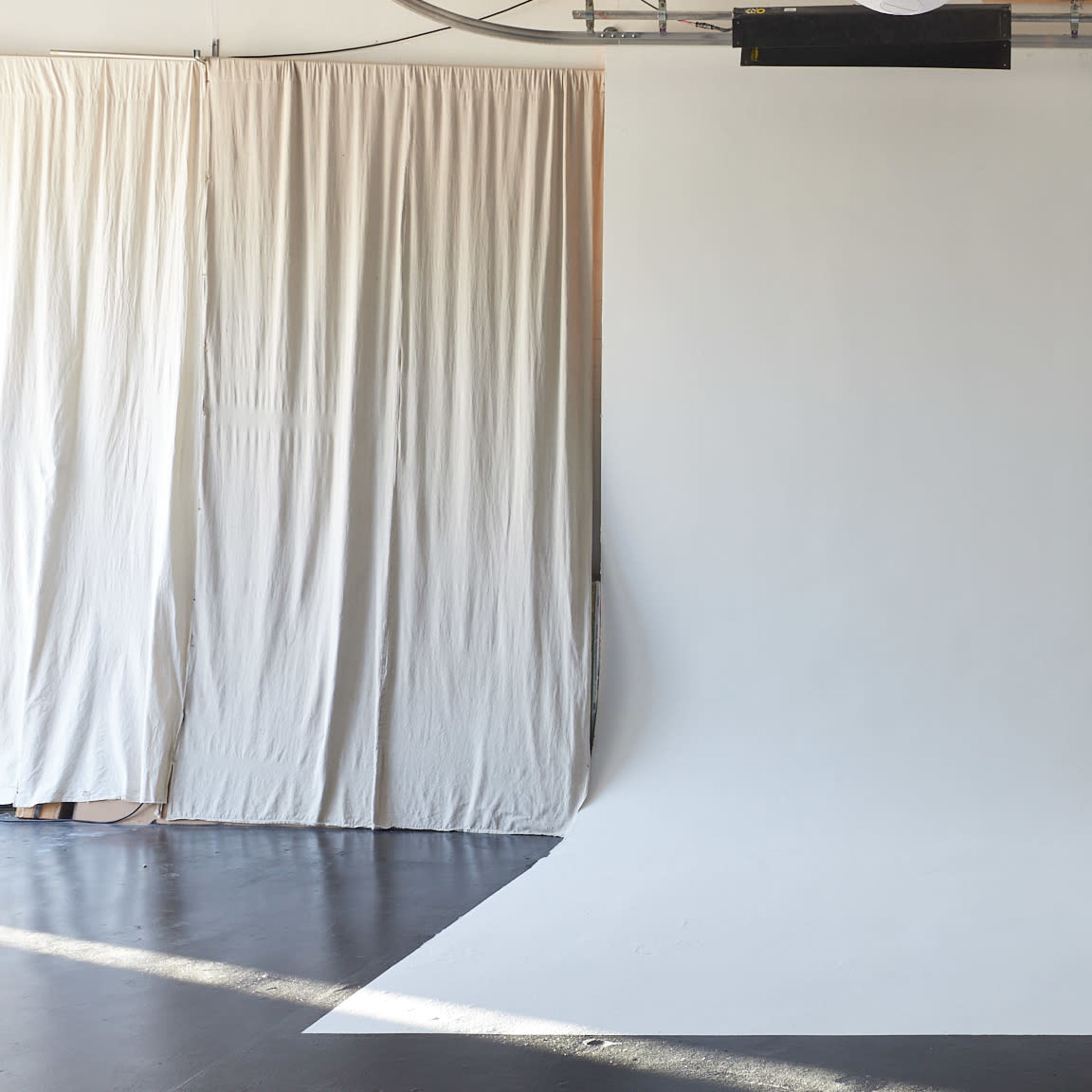 A spacious studio with a white backdrop and curtains on one side.