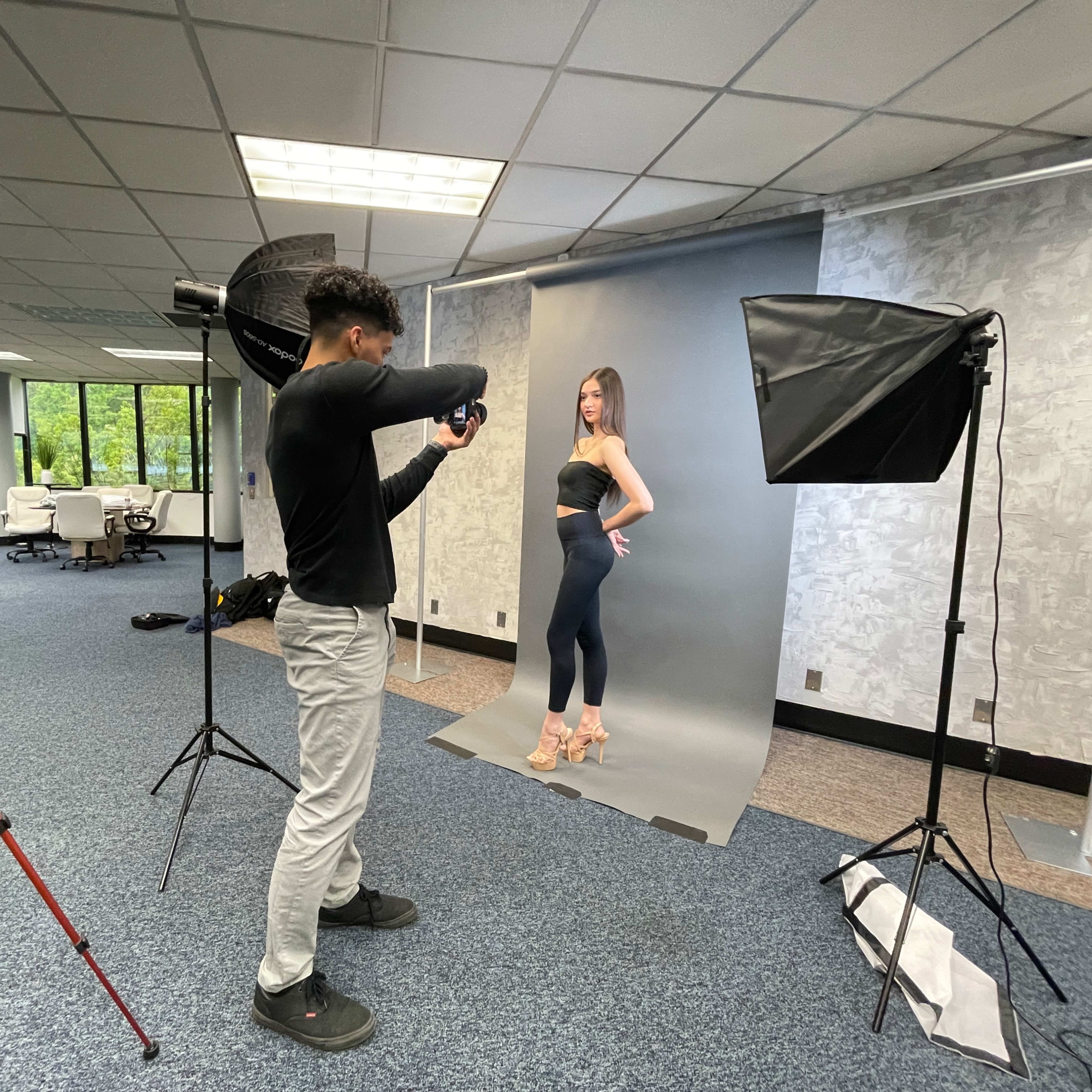 A photographer captures a model posing in front of a backdrop in a spacious studio.