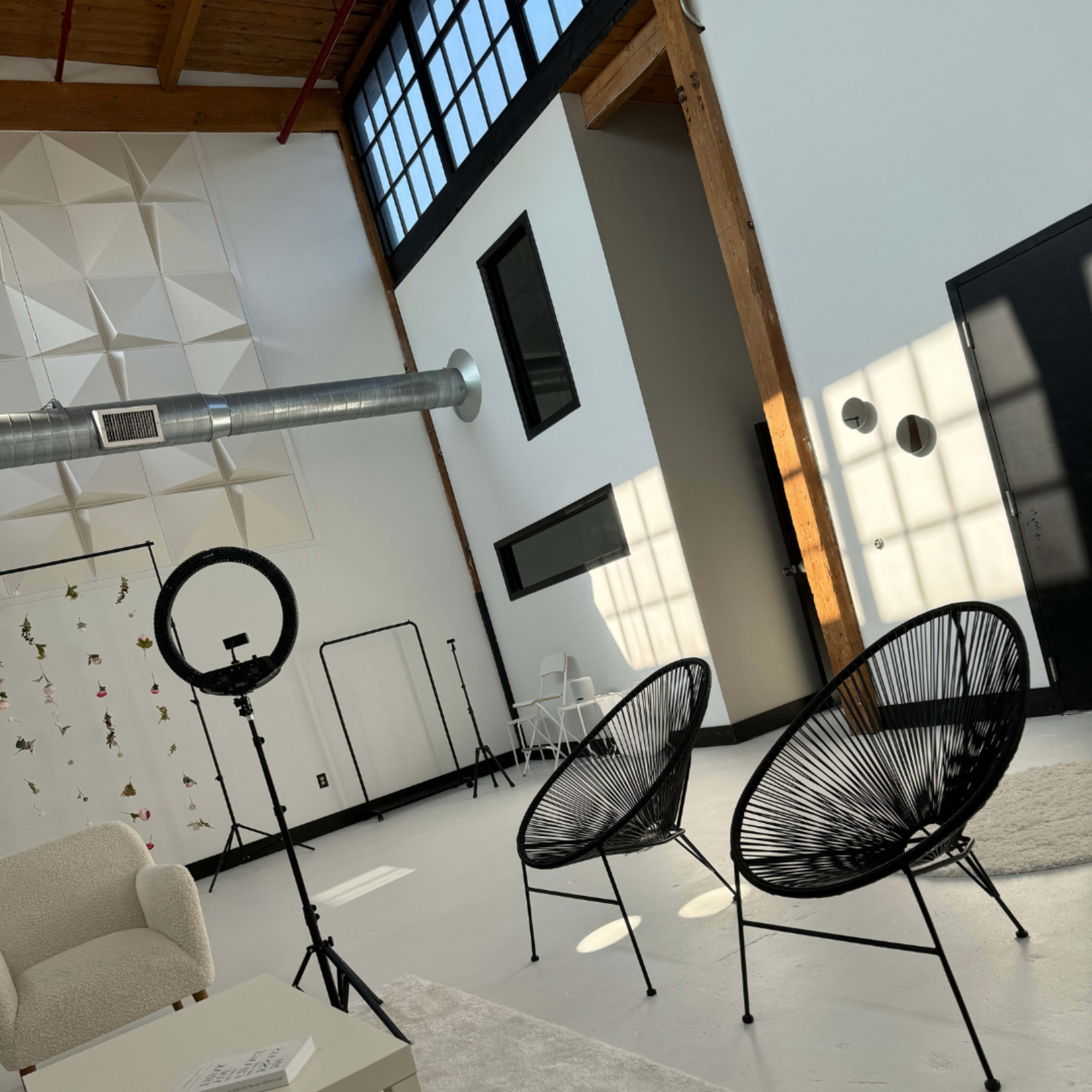 A bright, modern interior featuring two black wire chairs, a white table, and large windows.