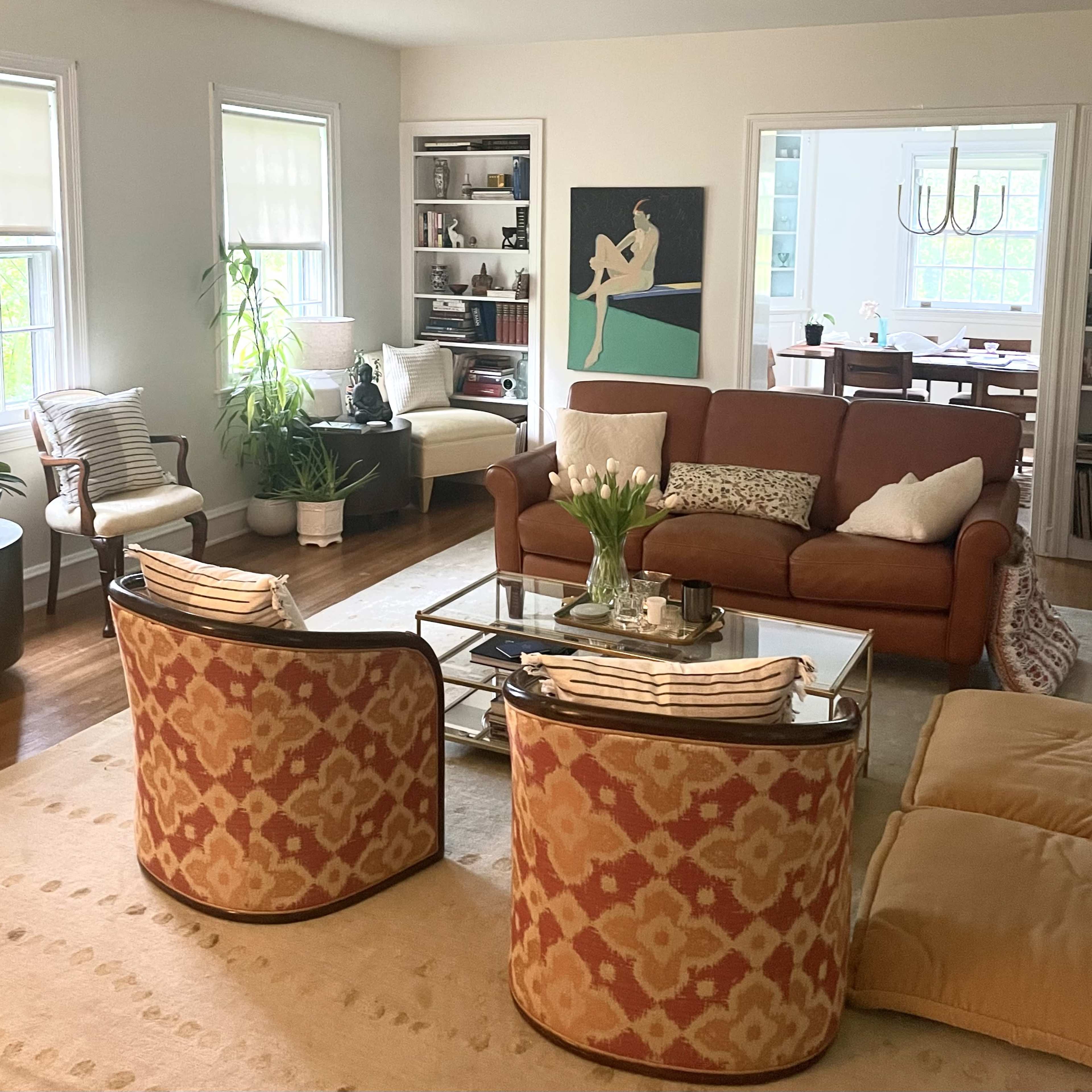 A bright living room with a brown sofa, two patterned chairs, a coffee table, and large windows allowing natural light.