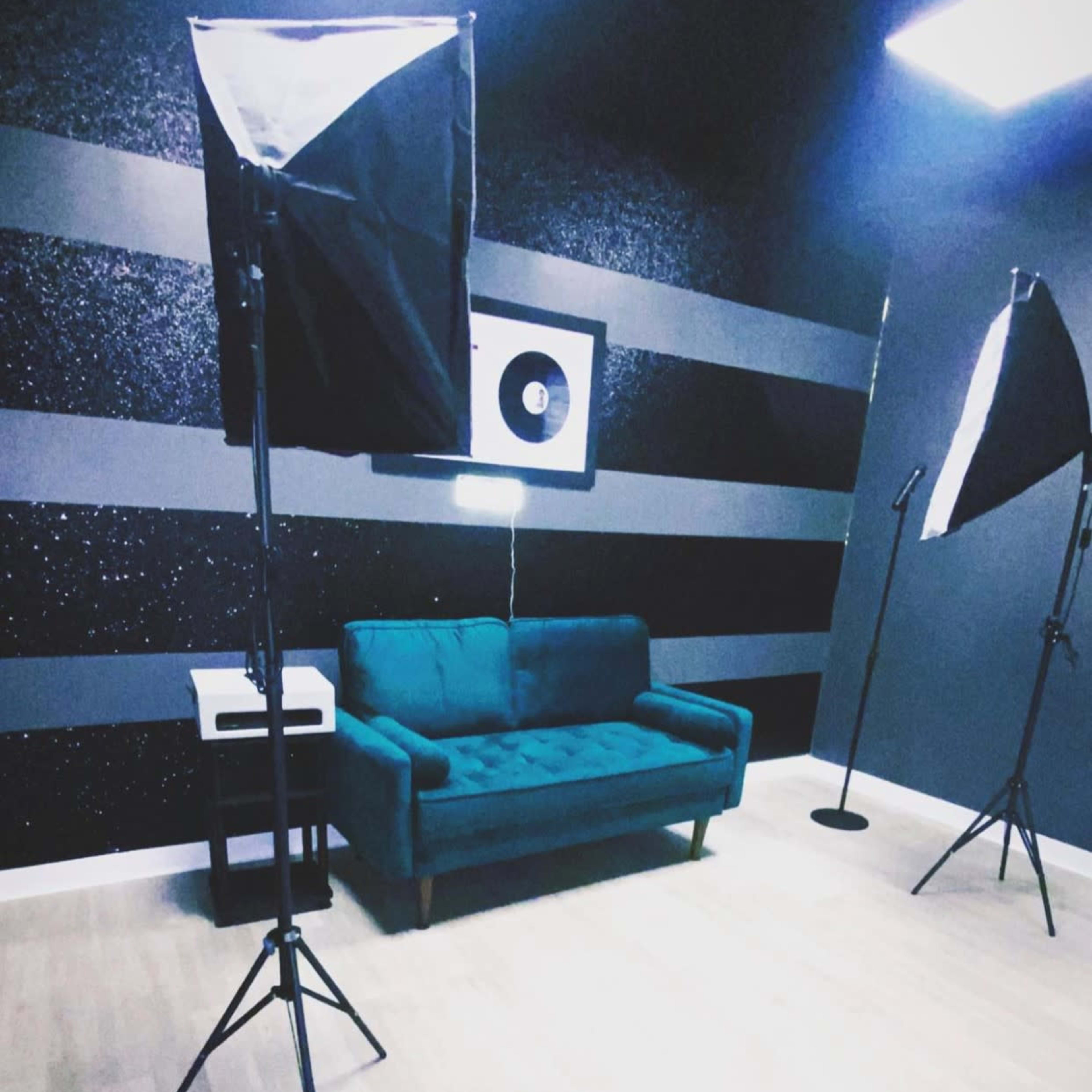 A photography studio with a teal couch, softbox lights, and a framed vinyl record on the wall.