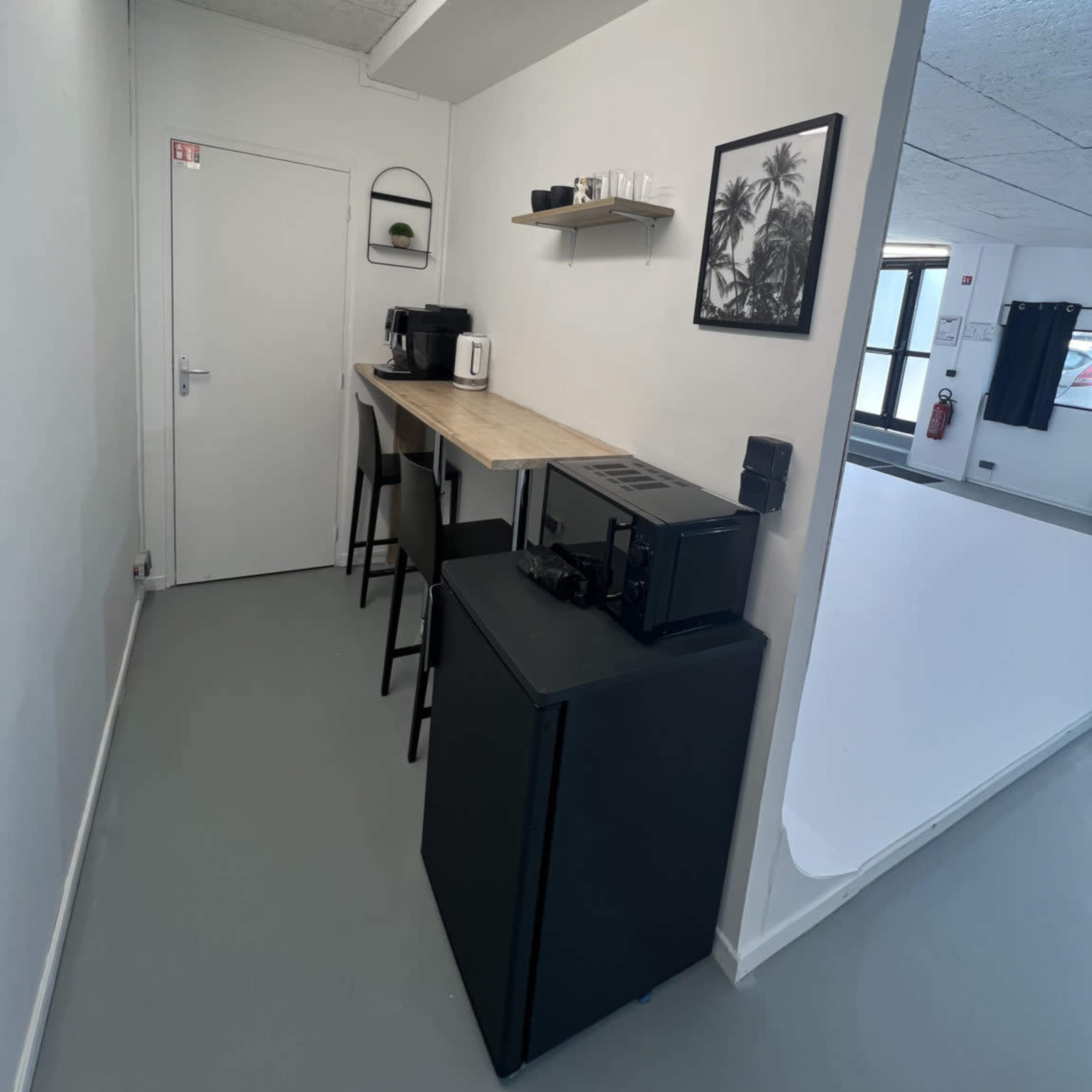 A kitchenette area features a wooden countertop with bar stools, coffee machines, and a microwave, alongside a door leading to another room.