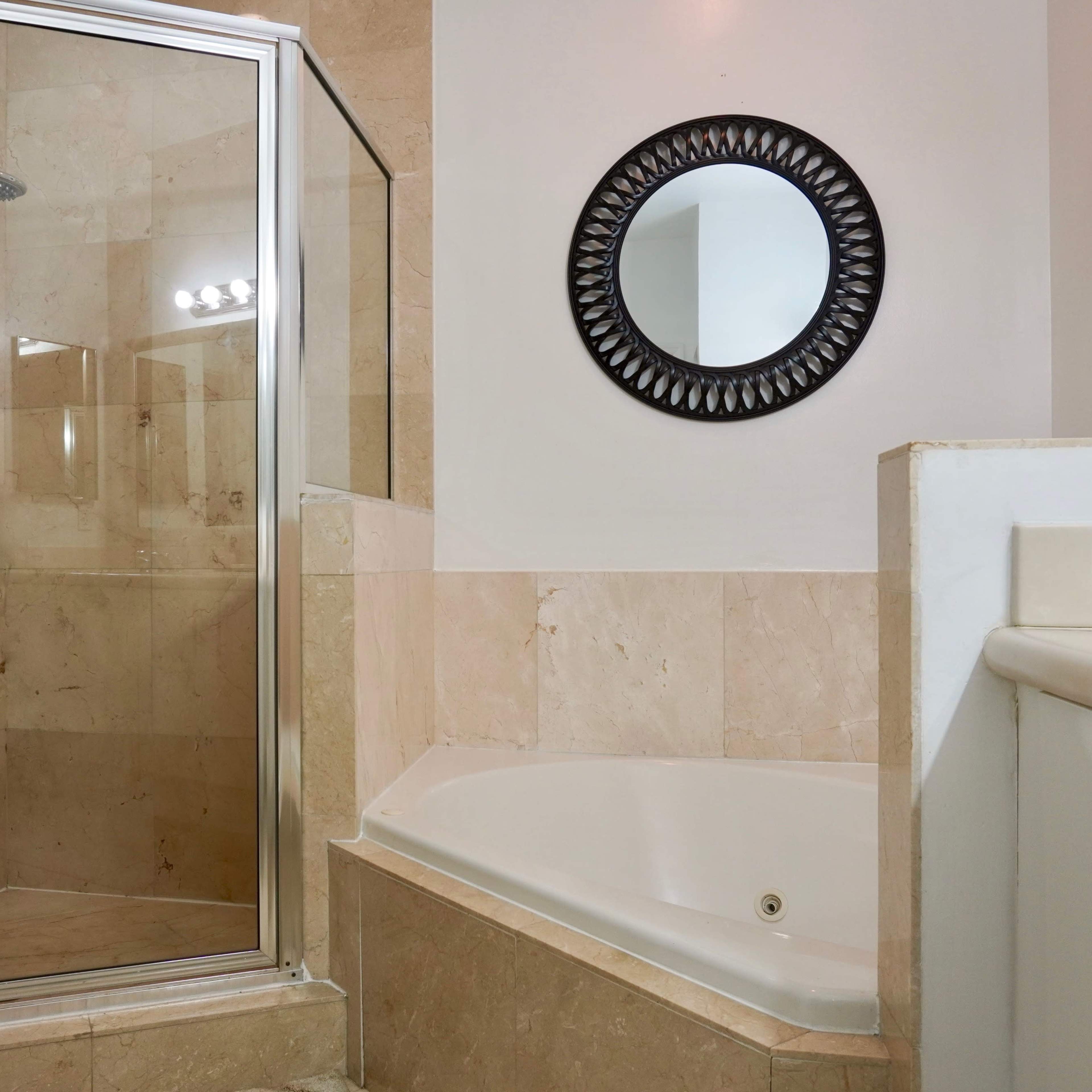A bathroom featuring a glass-enclosed shower, a bathtub, and a round mirror on the wall.