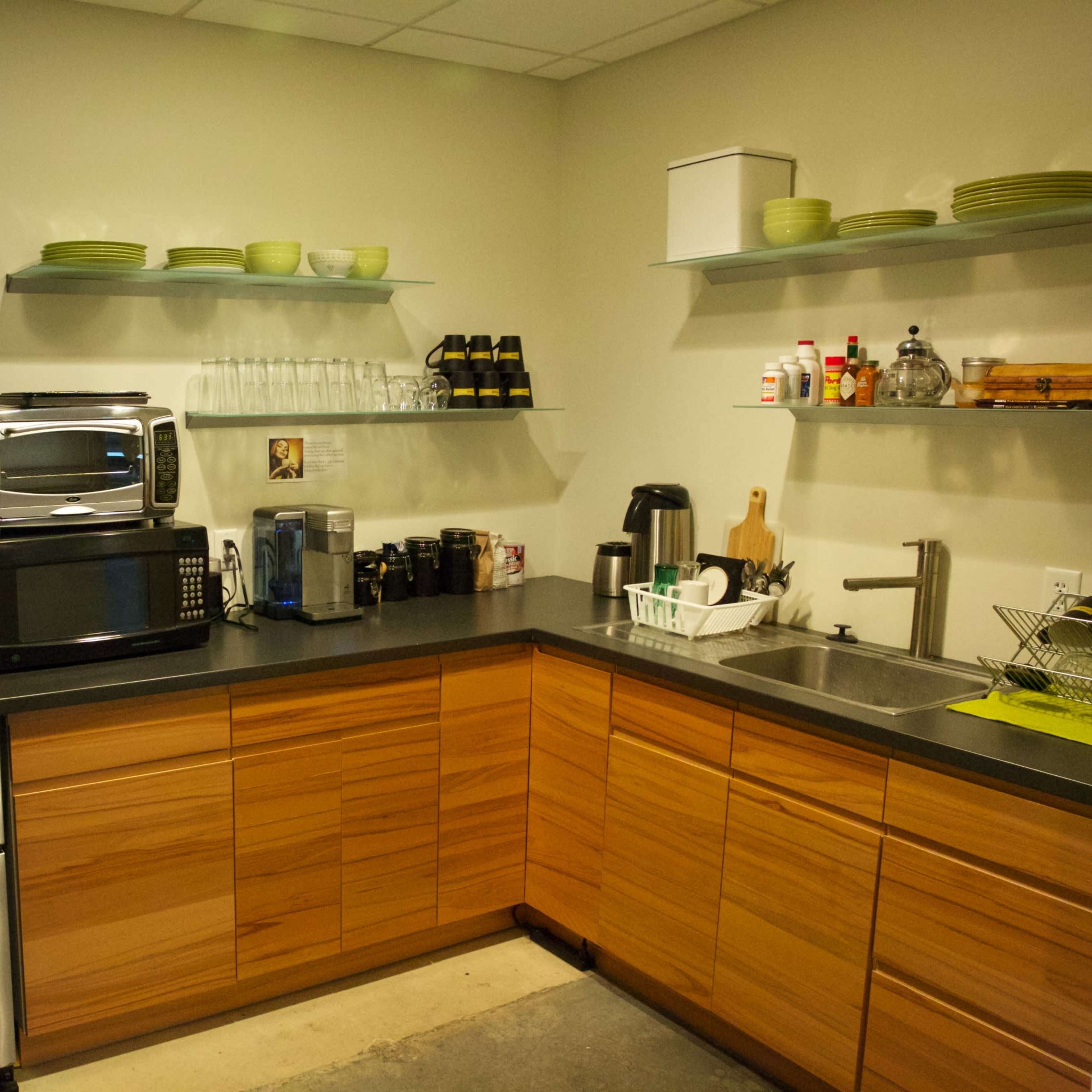 A modern kitchen with stainless steel appliances, wooden cabinets, glassware on shelves, and a sink area.