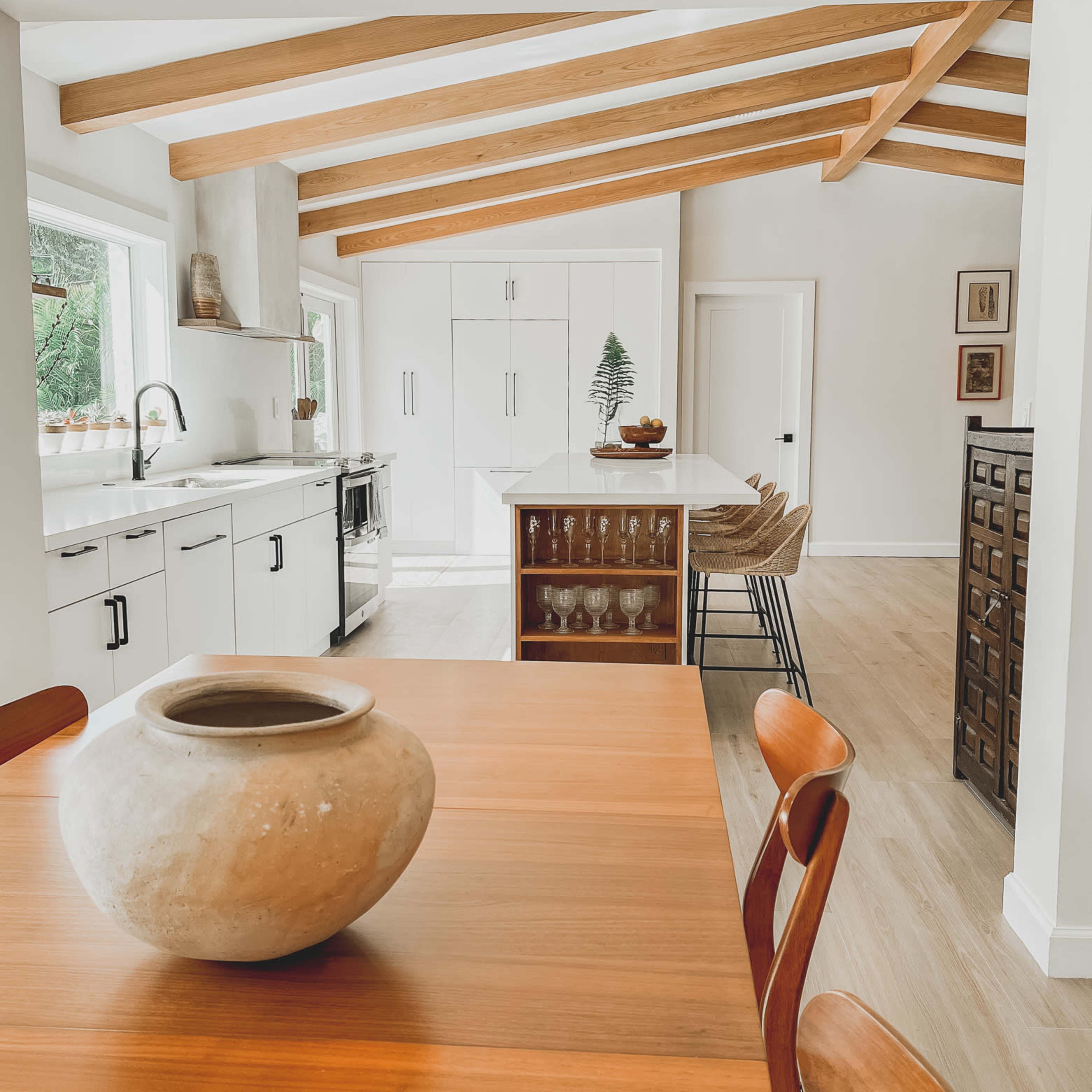 A modern kitchen with wooden beams, a dining table in the foreground, and sleek cabinetry in the background.