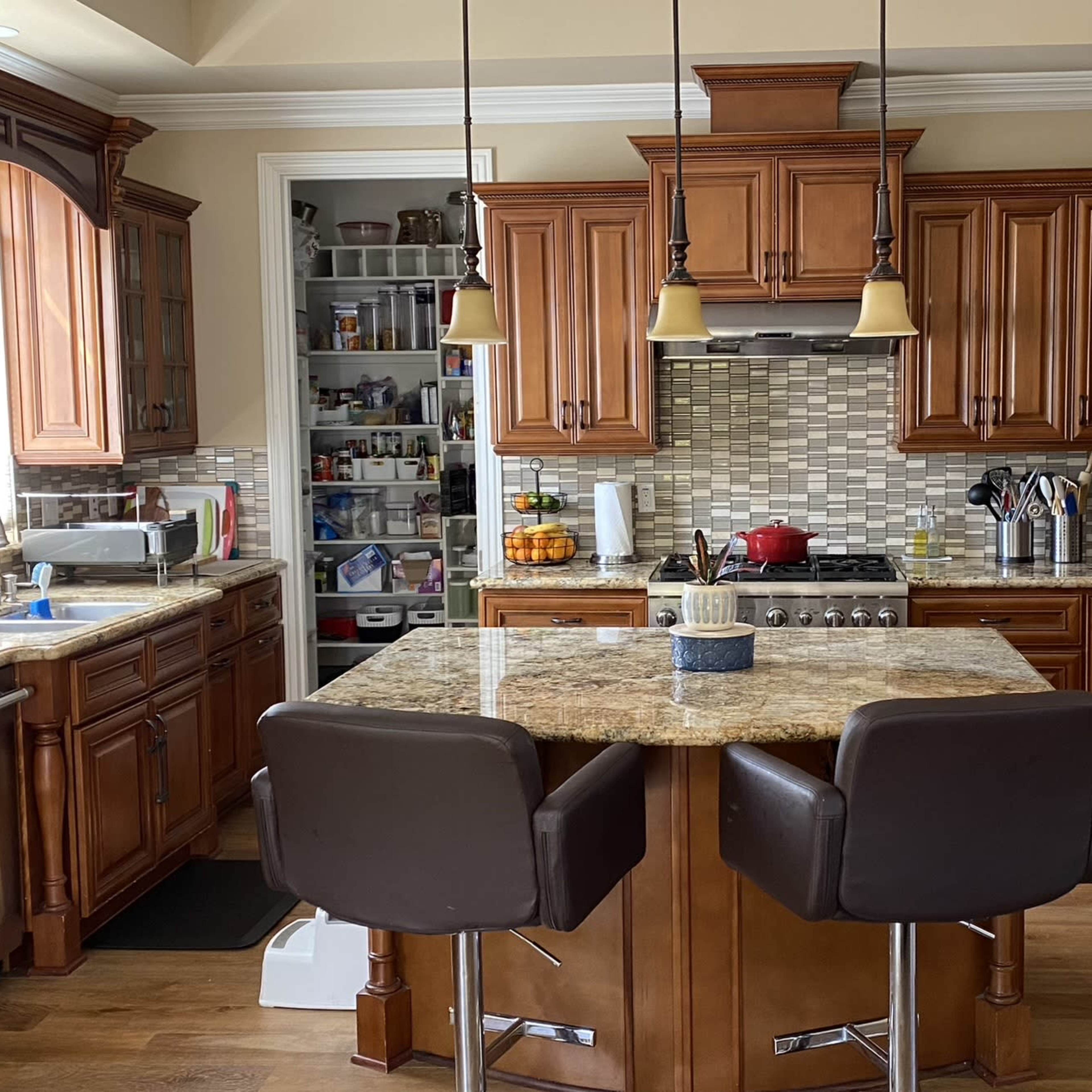 A kitchen with wooden cabinetry, granite countertops, and a central island with two chairs.