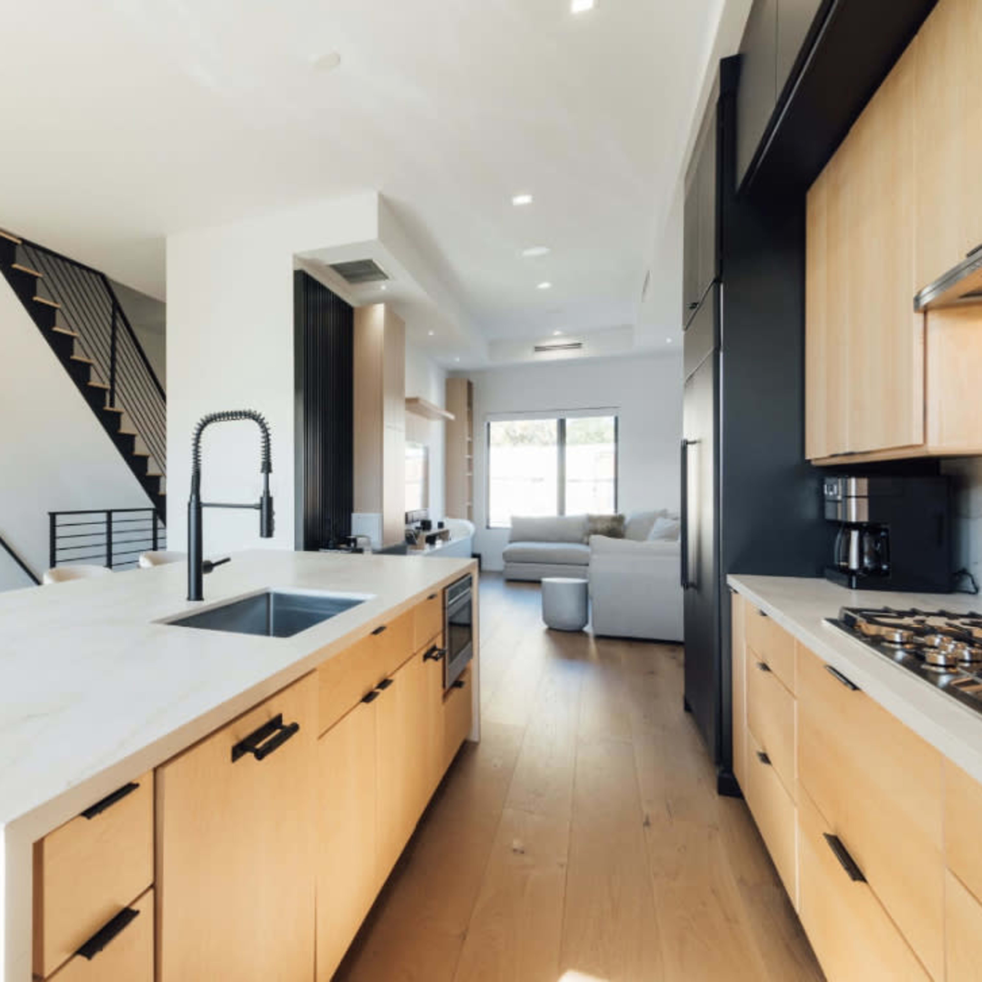 A modern kitchen with light wood cabinetry, a large marble island, and an open layout leading to a living area.
