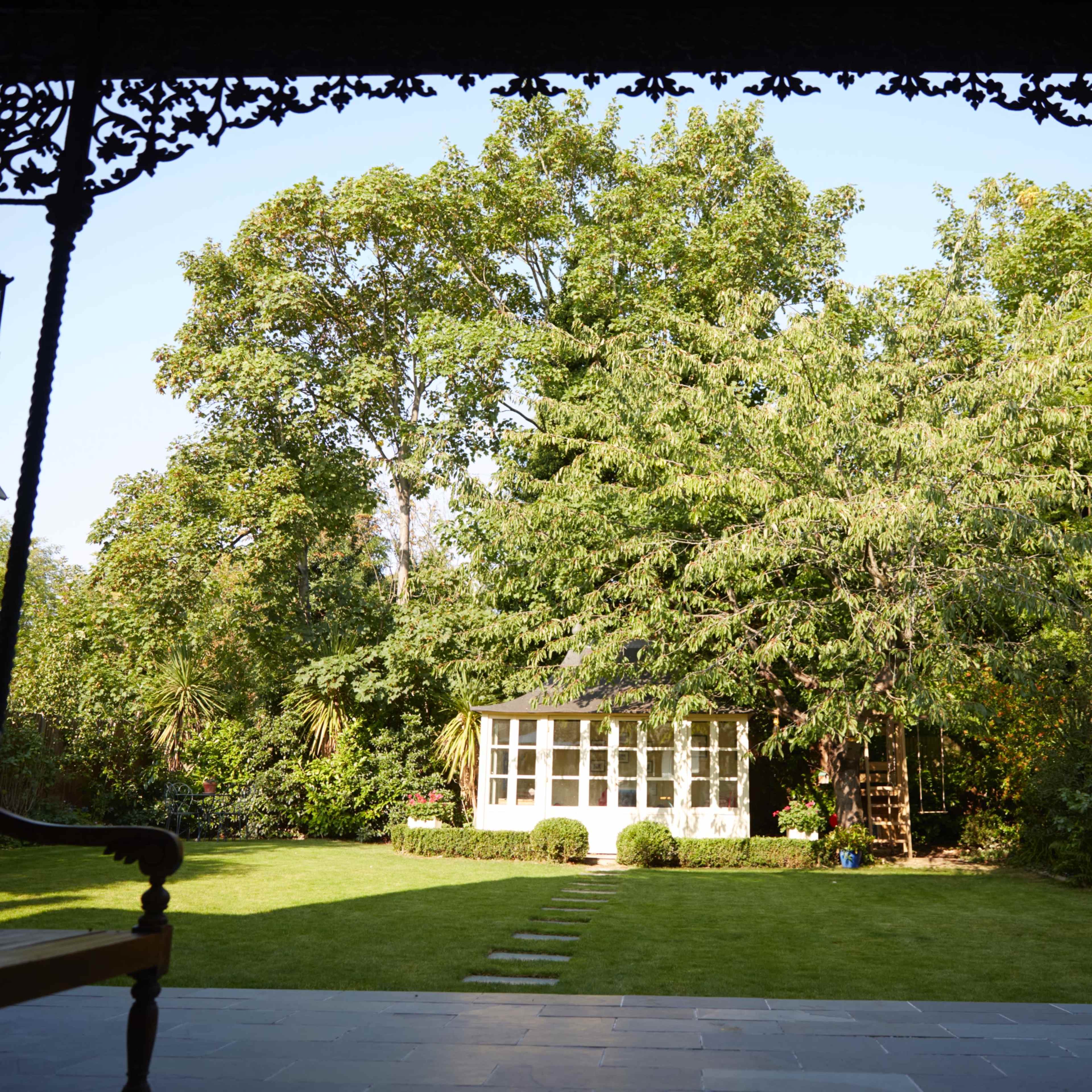 A spacious garden with a well-maintained lawn, featuring a glass-walled gazebo and a large tree.