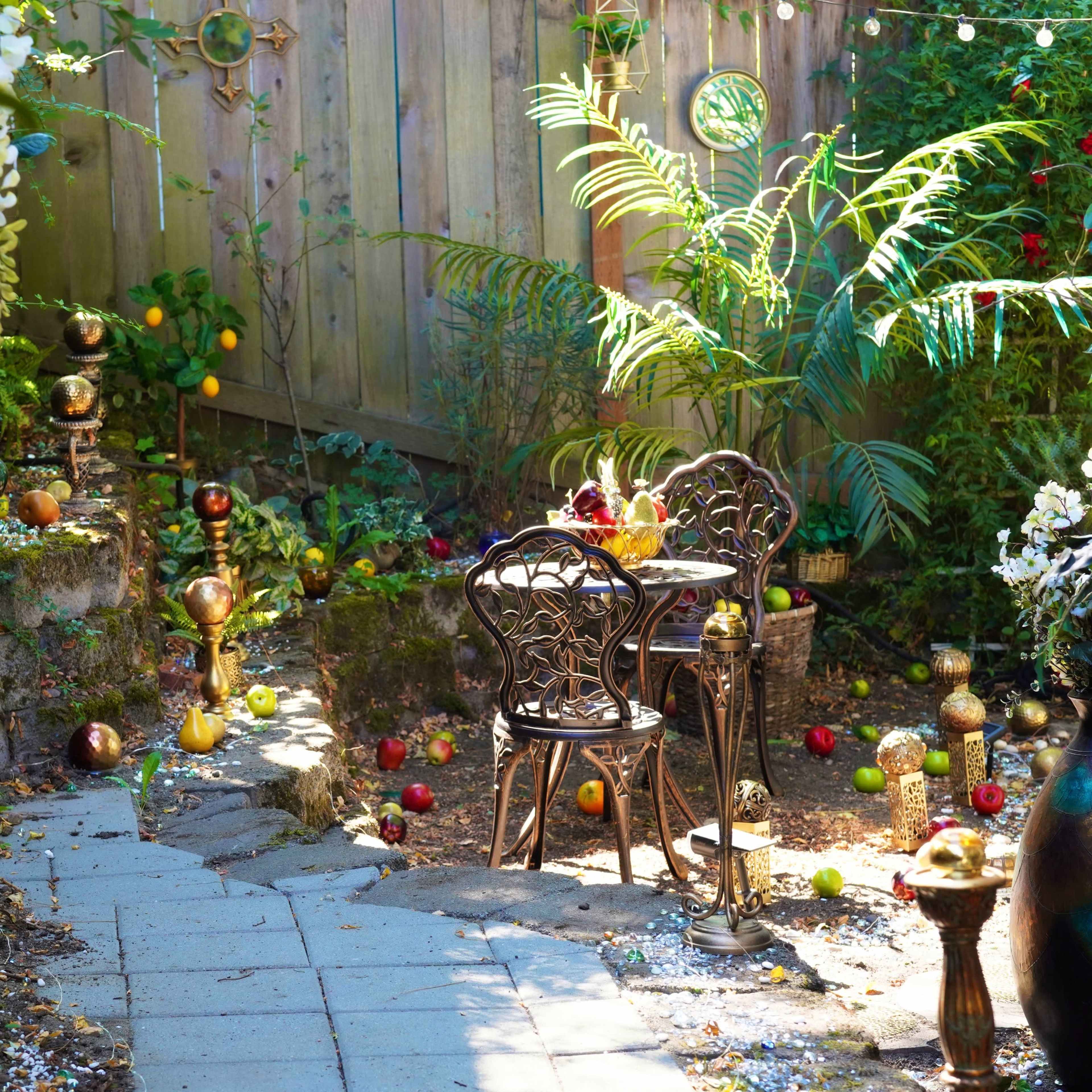 A small garden features a stone pathway leading to a wrought iron table and chairs surrounded by colorful decorations.