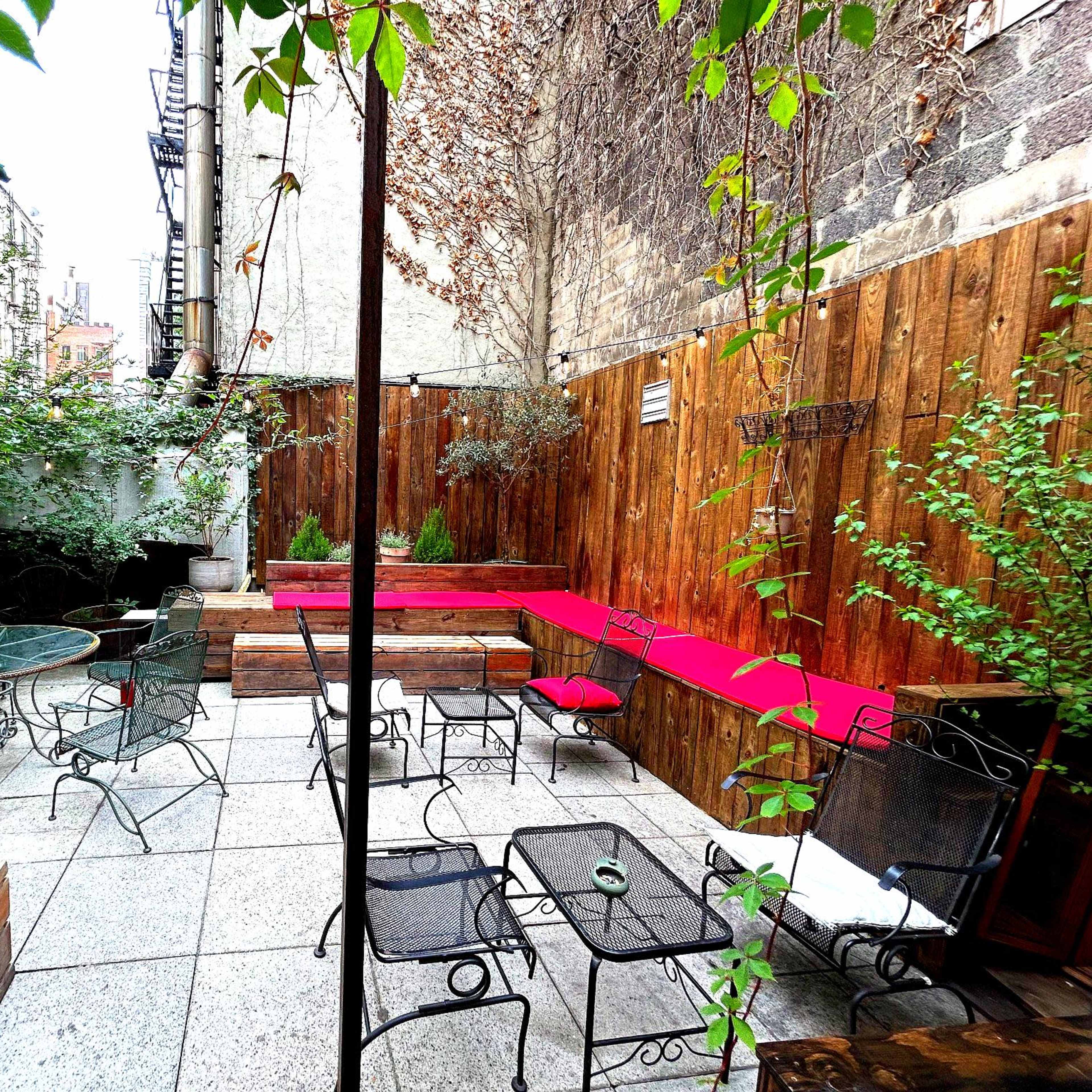 A small, enclosed outdoor courtyard with wooden walls, metal furniture, and greenery.