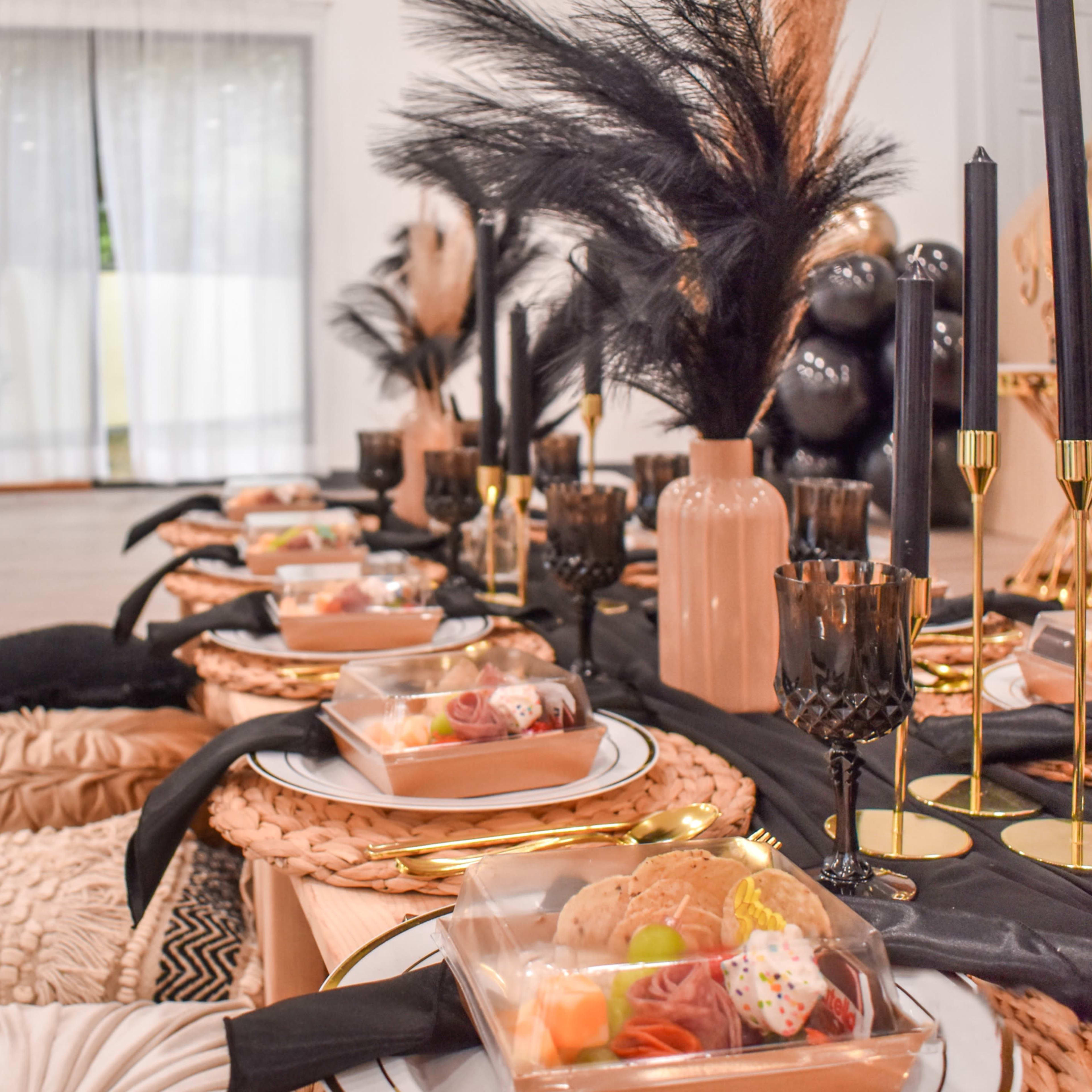 A beautifully arranged dining setup features neatly placed trays of food, elegant black candles, and decorative elements on a long table.