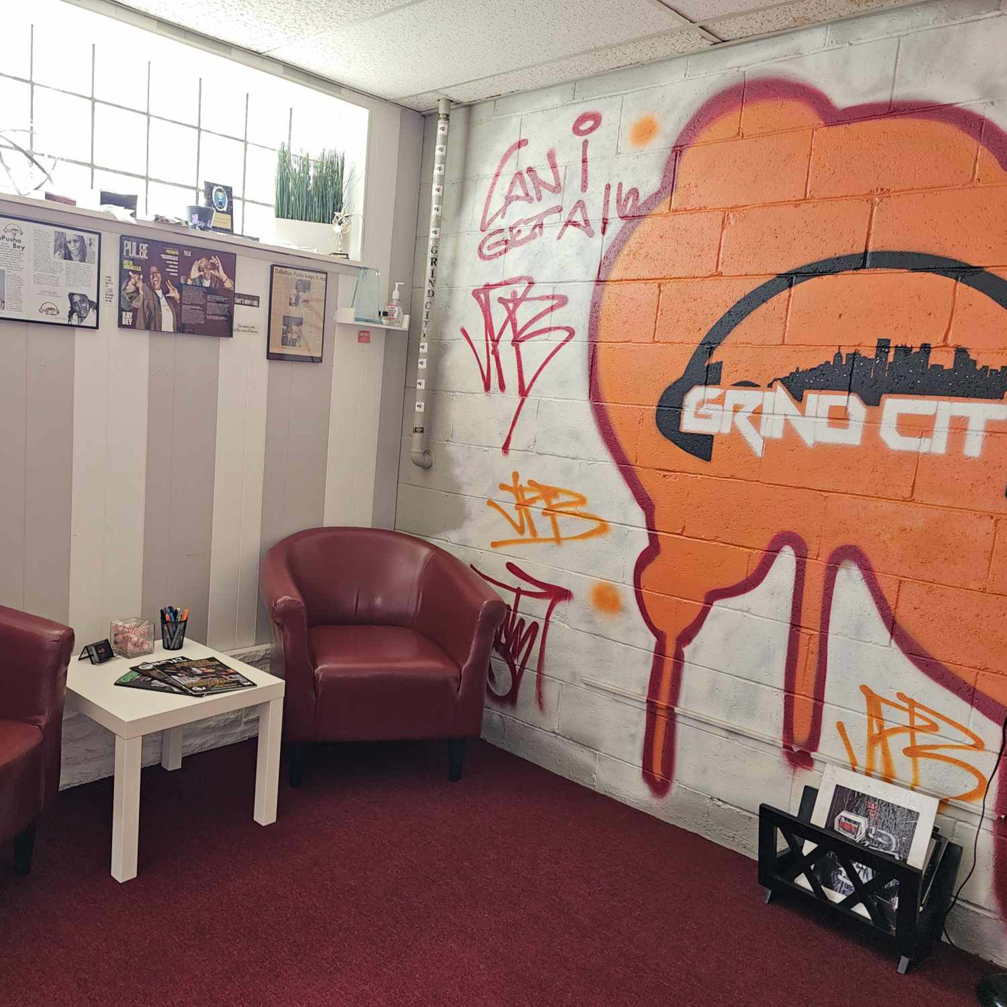 A small waiting area with two red chairs, a white table, and a wall decorated with framed articles and graffiti.