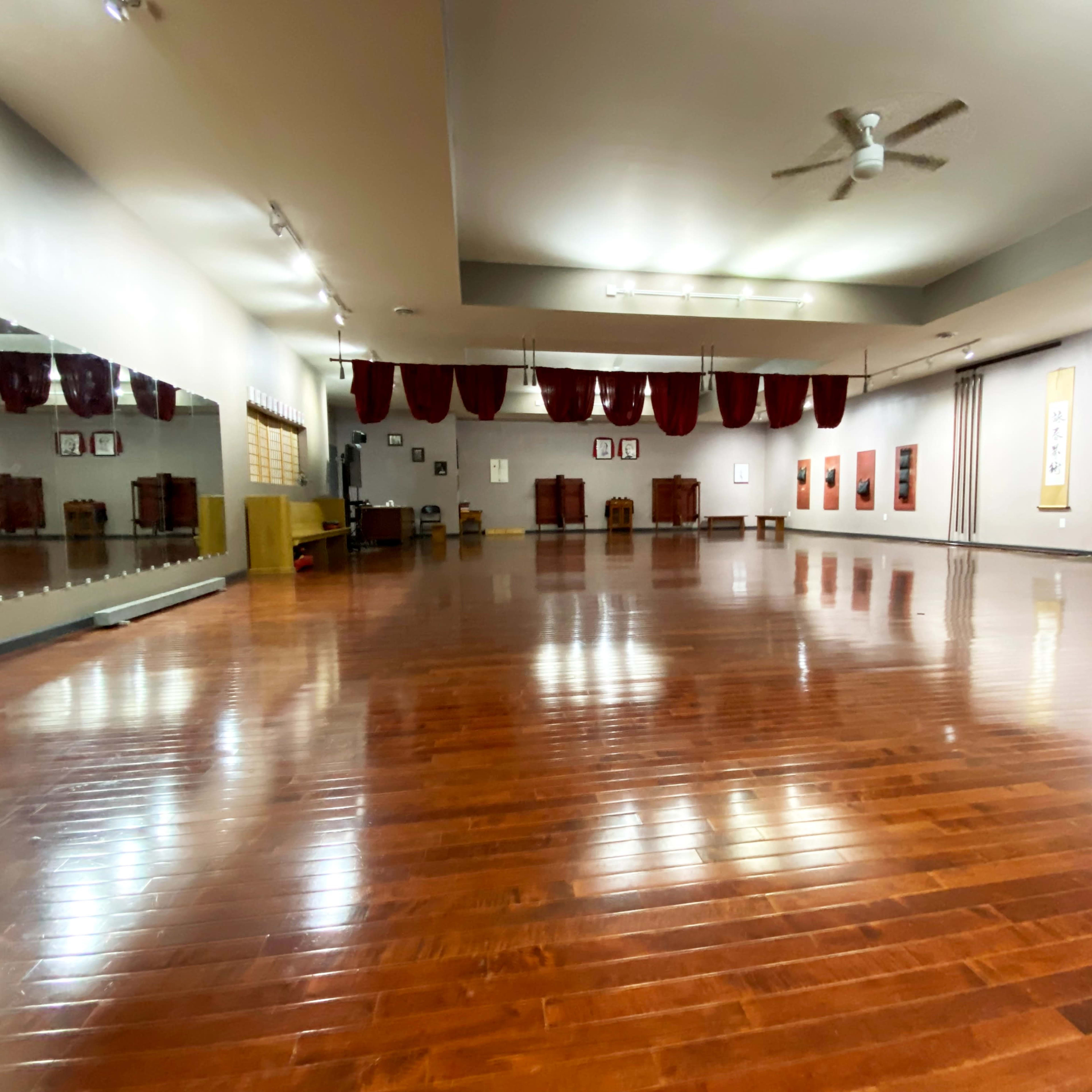 A spacious, empty studio with polished wooden floors, mirrors on one wall, and red curtains draped along the ceiling.