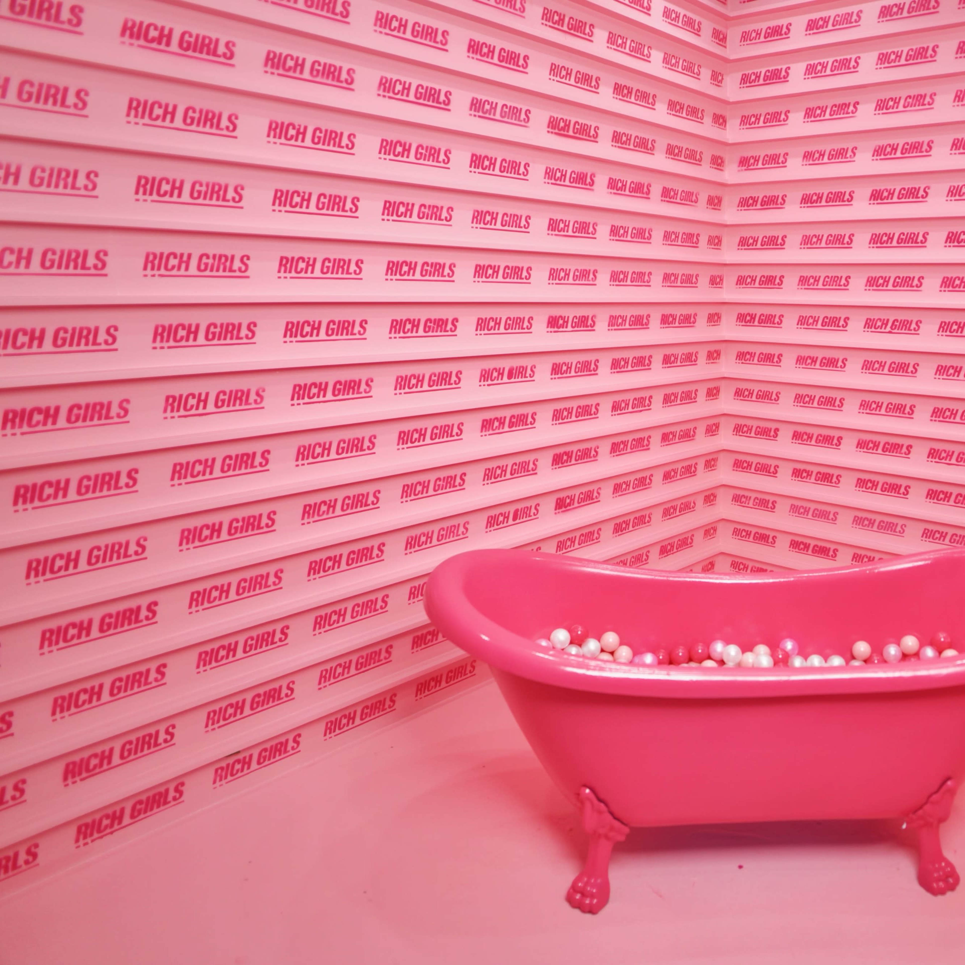 A pink bathtub filled with white balls is placed against a background of repeating pink panels that say "RICH GIRLS."