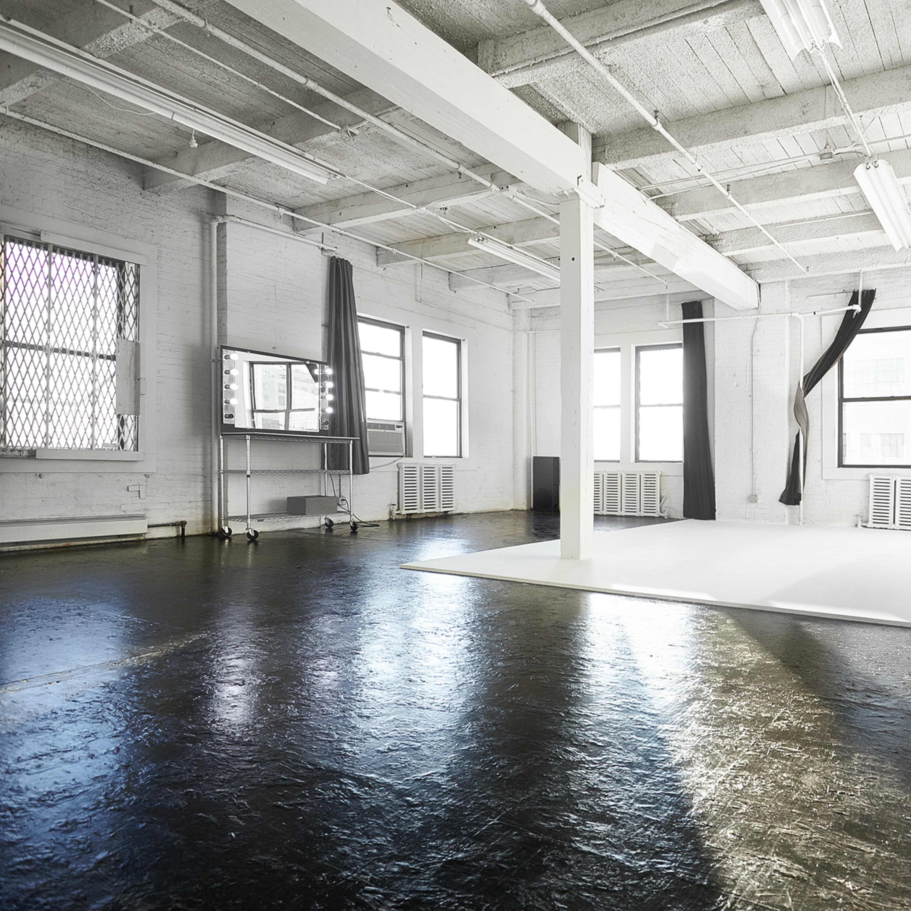 A spacious, well-lit studio with large windows, a curved white backdrop, and polished dark floors.