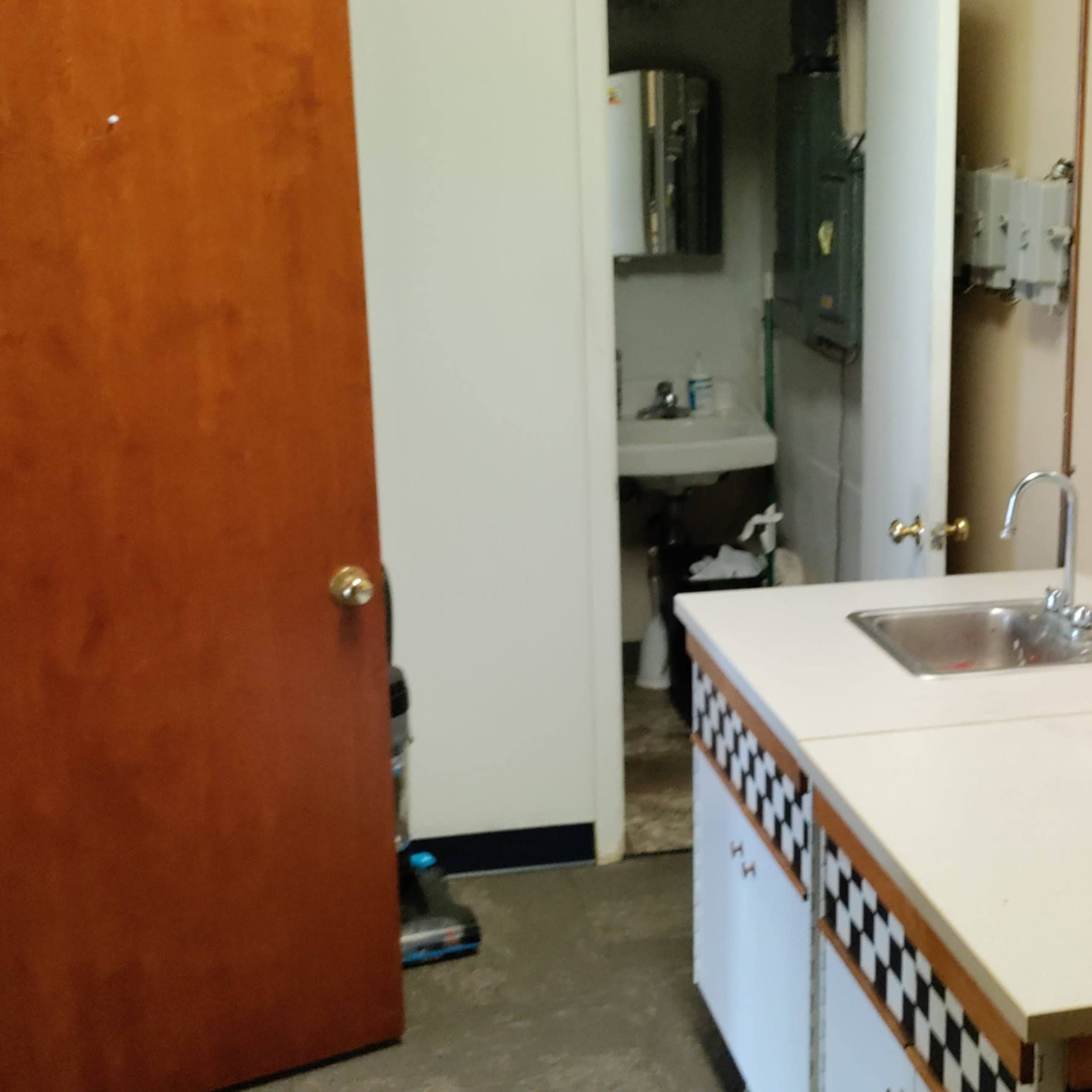 A small kitchenette with a microwave, sink, and a door leading to a restroom area.