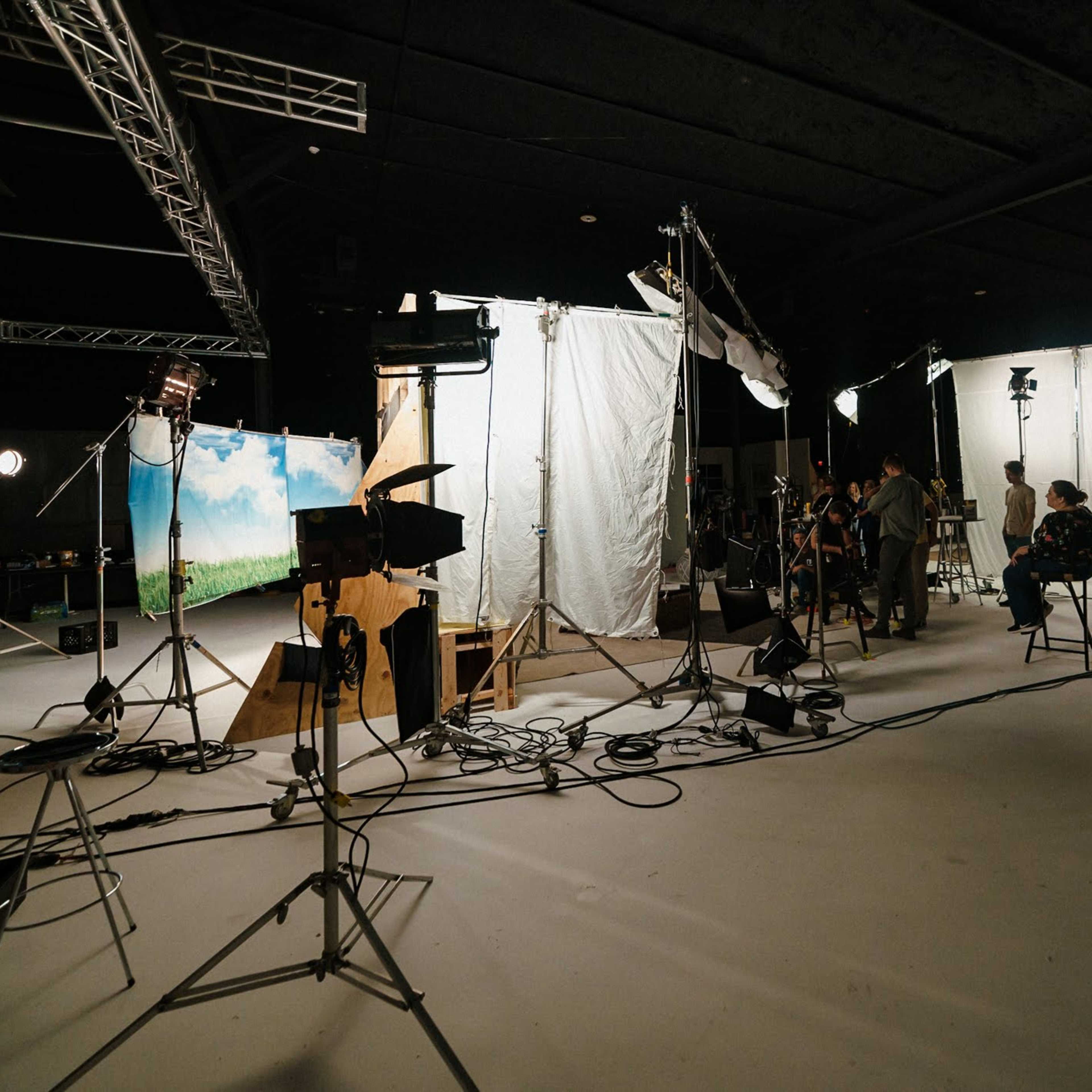 A film set is arranged with lighting equipment, staging backdrops, and crew members preparing for a shoot.