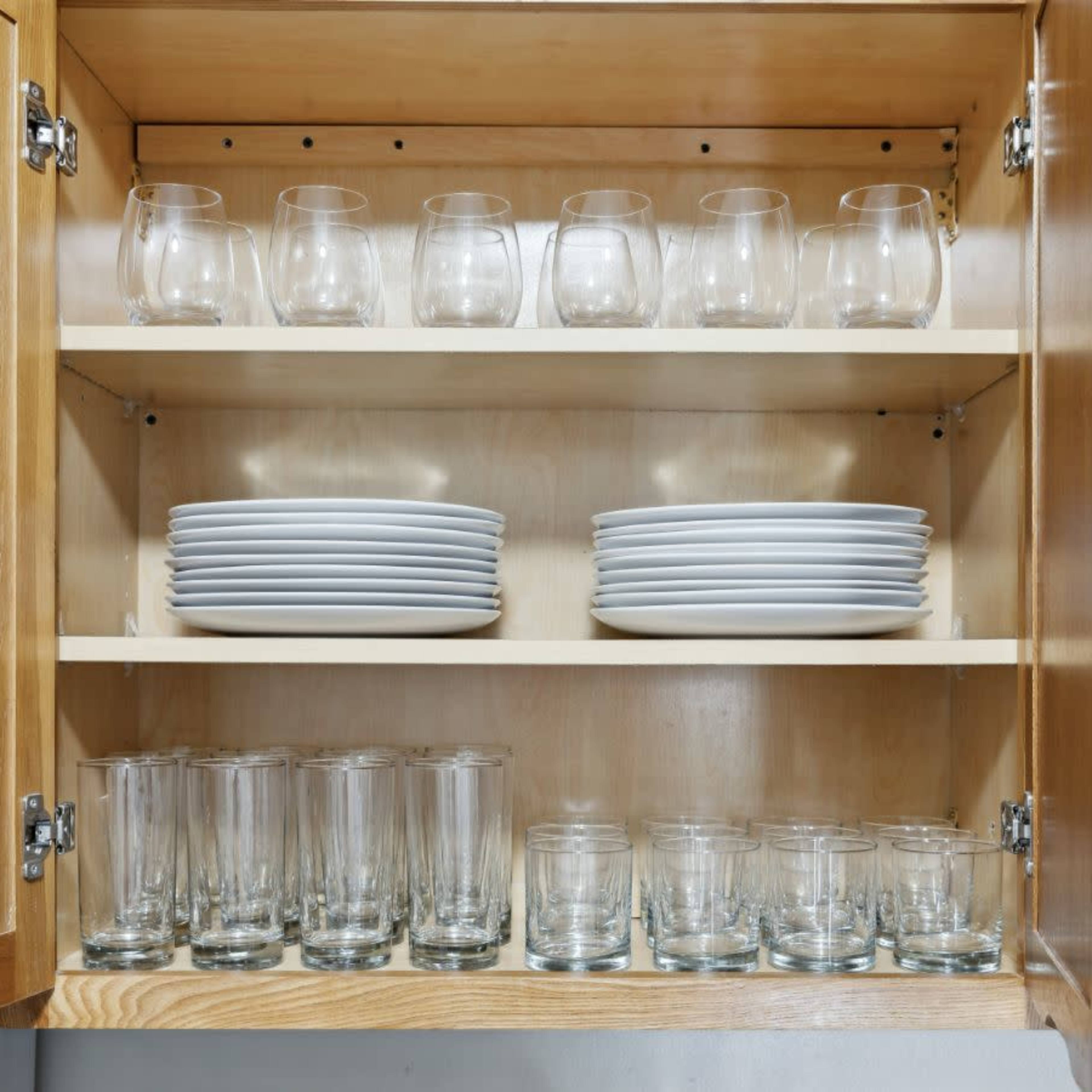 A wooden kitchen cabinet with neatly organized glassware and plates on two shelves.