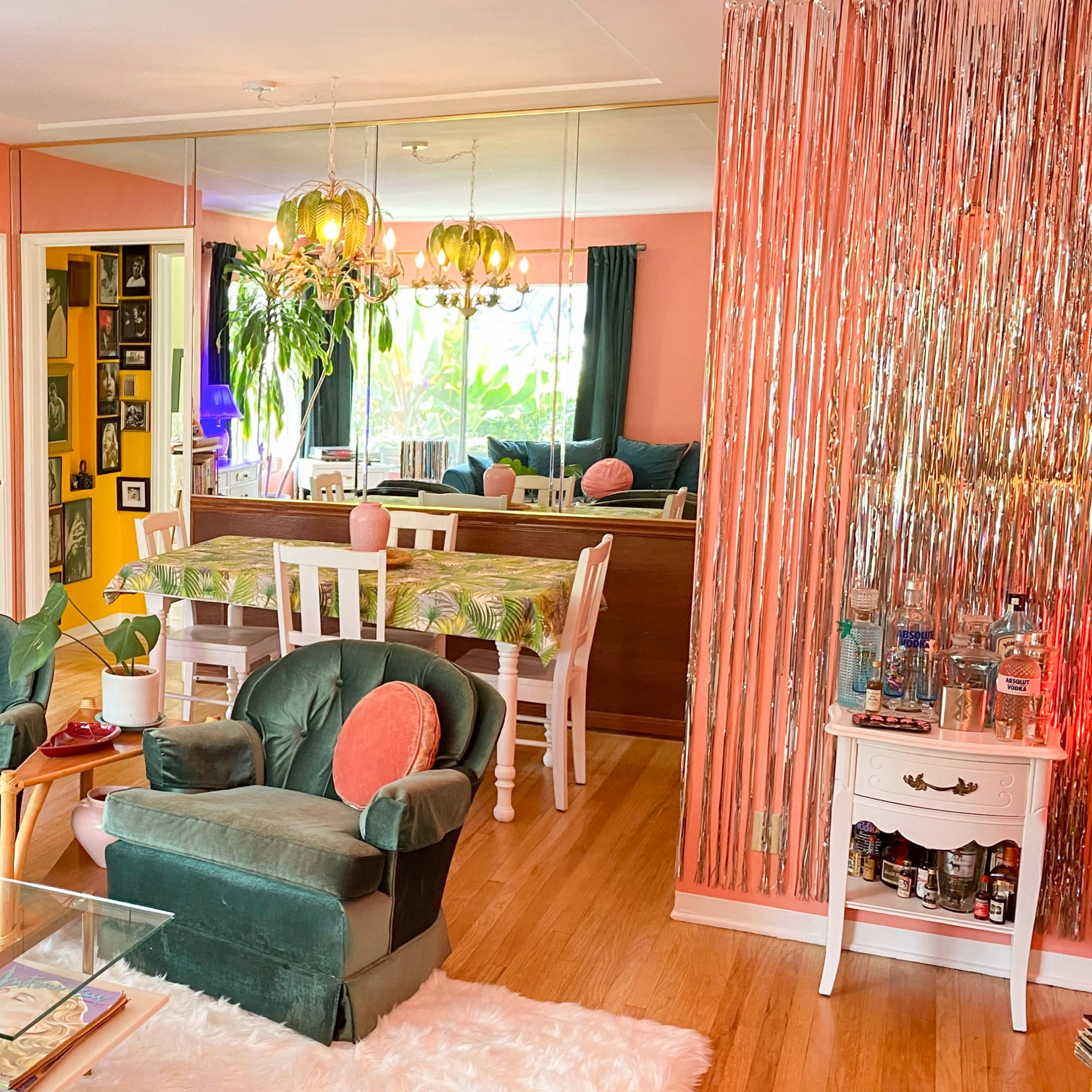A bright living room with green velvet chairs, a glass coffee table, and vibrant decor, including plants and colorful wall art.