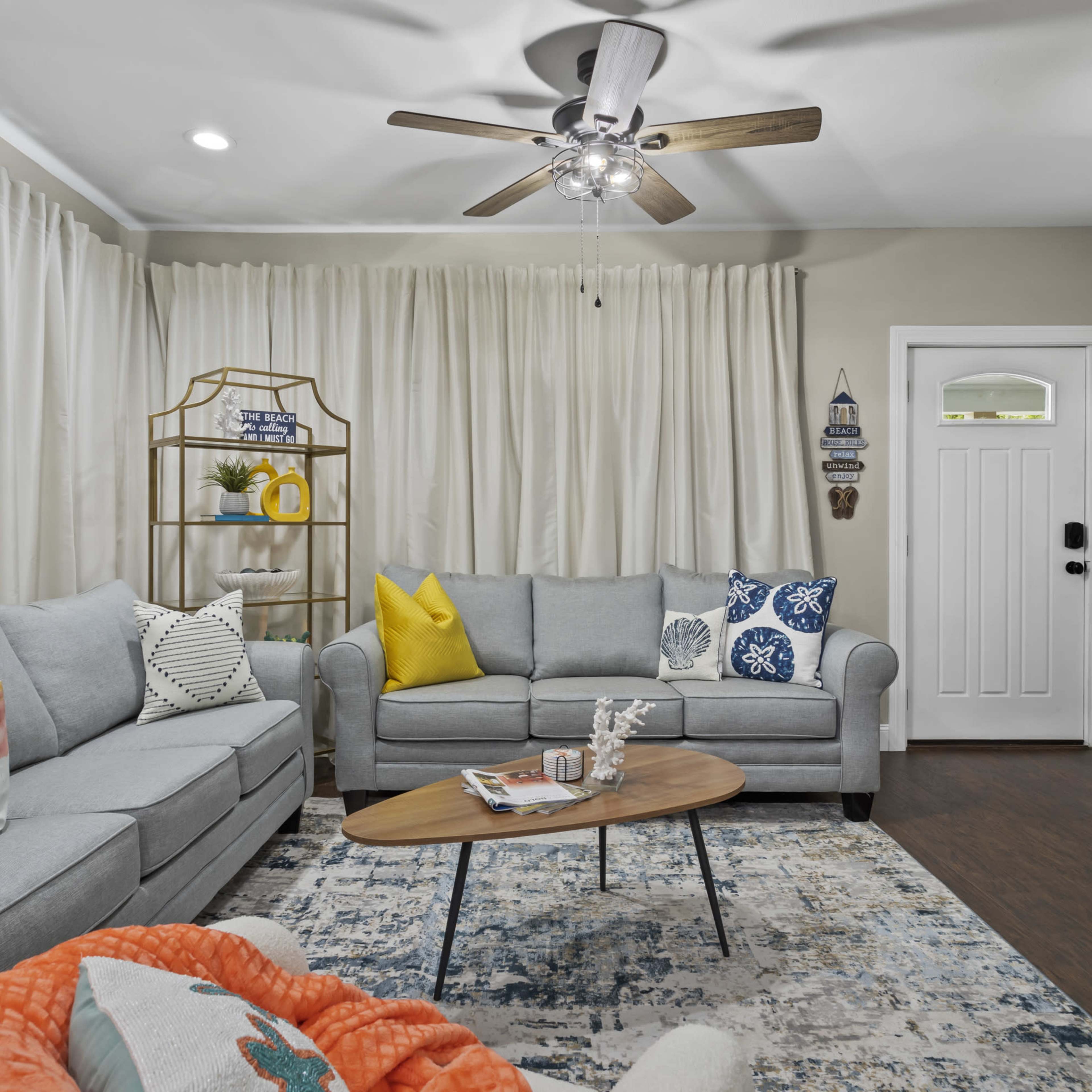 A cozy living room with a light gray sofa, an orange throw blanket, a wooden coffee table, and a white door with a glass panel.