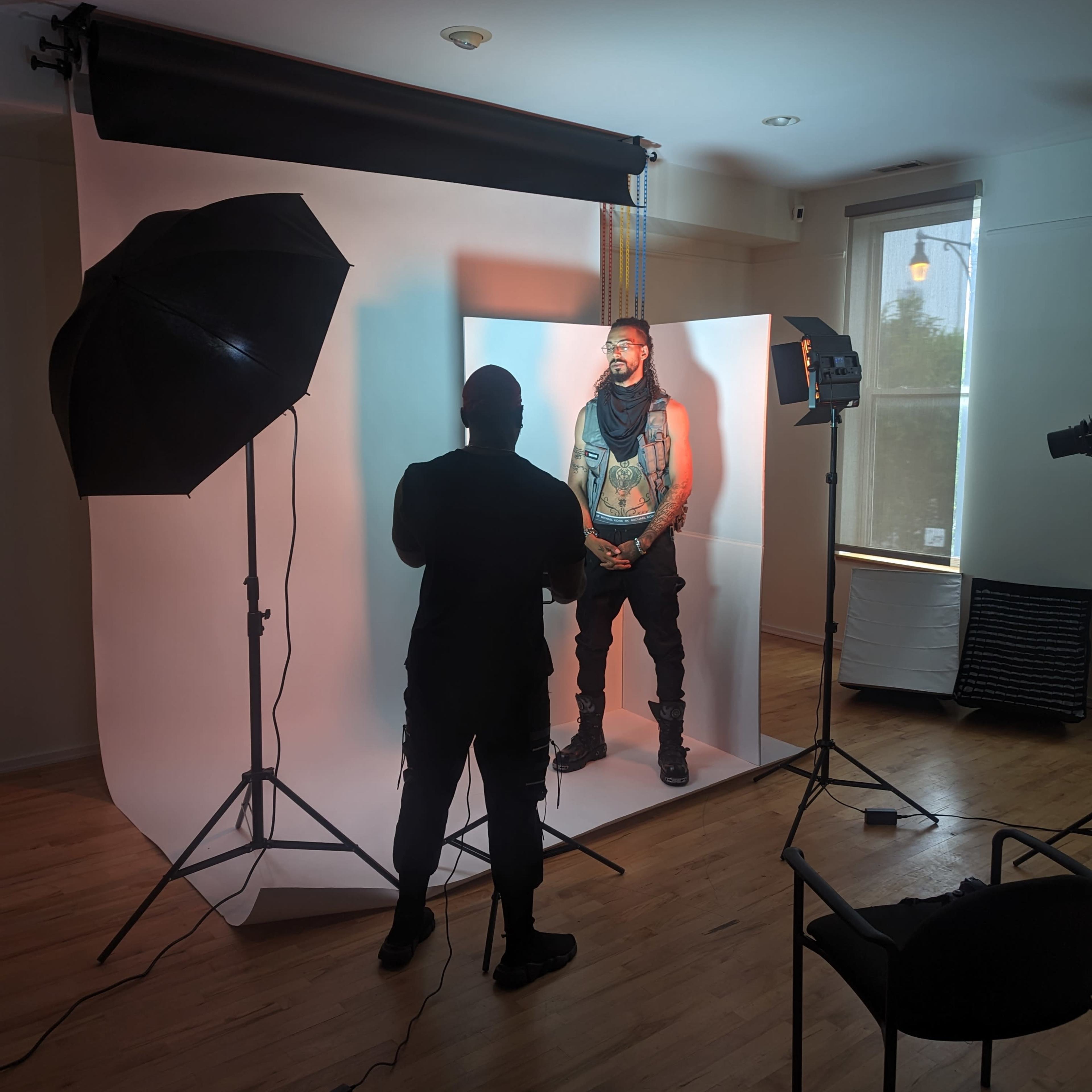 A photographer is capturing an image of a model standing against a white backdrop in a well-lit studio.
