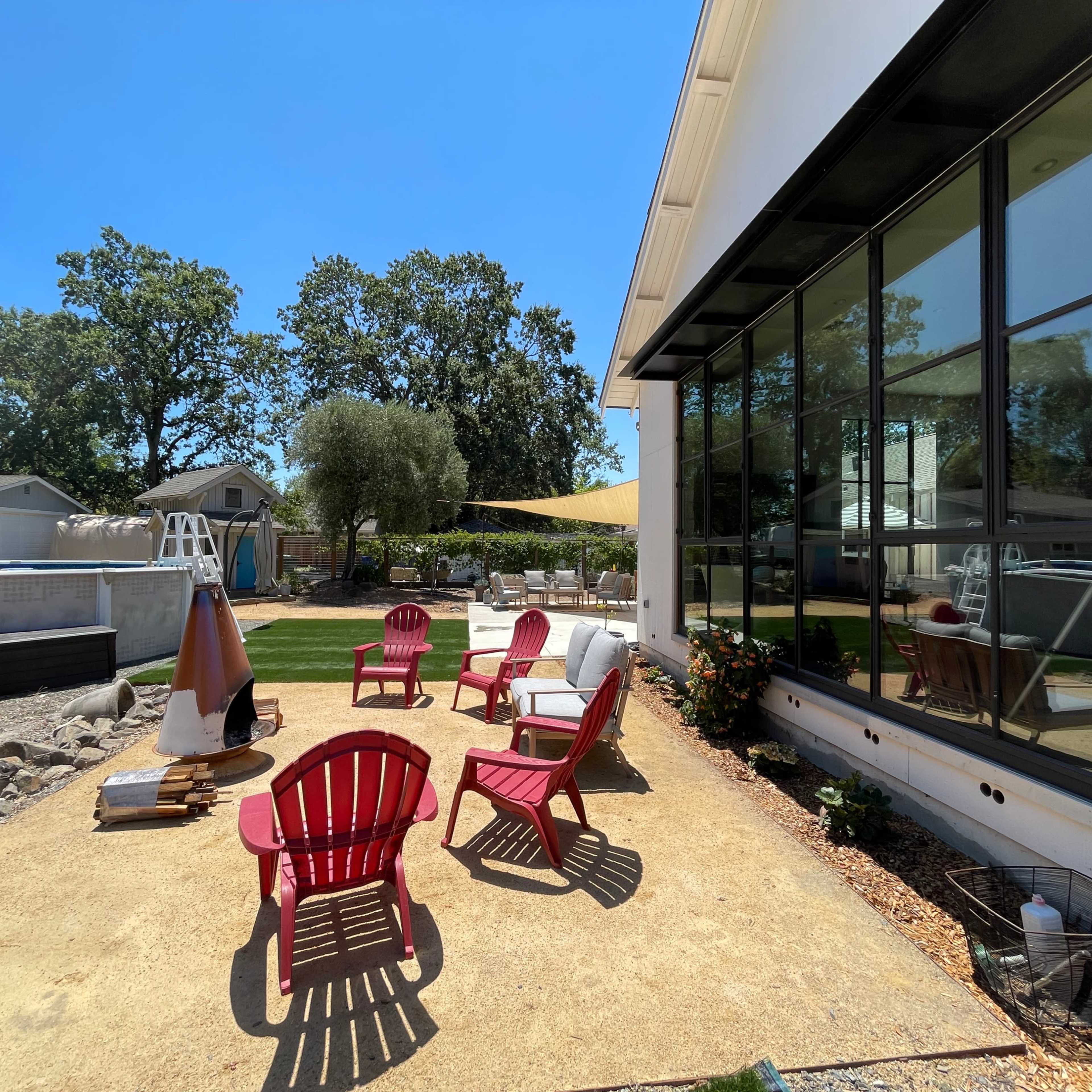 A backyard patio with pink adirondack chairs, a large window, and a grassy area in the background.