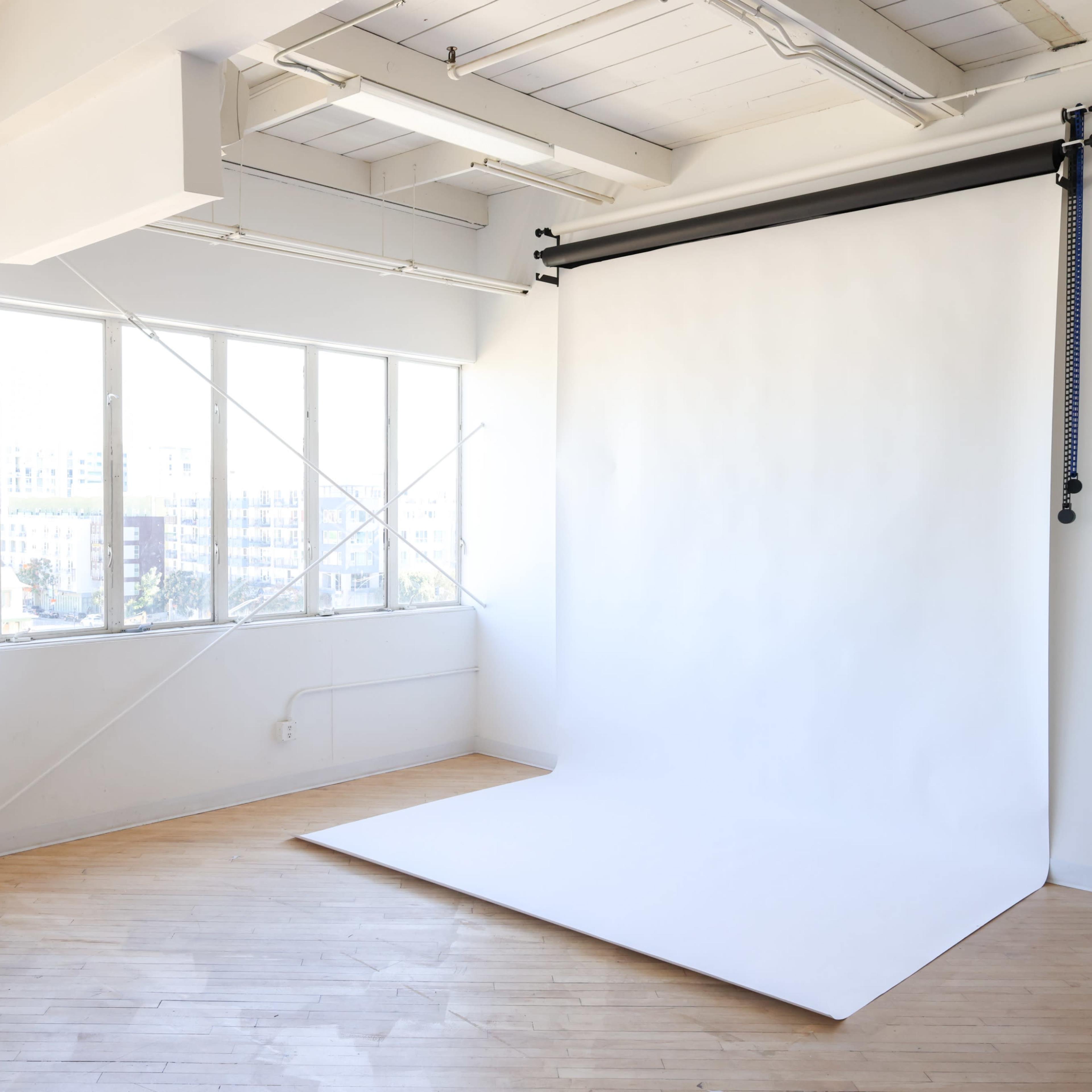 A spacious photography studio with large windows and a white backdrop on the side.