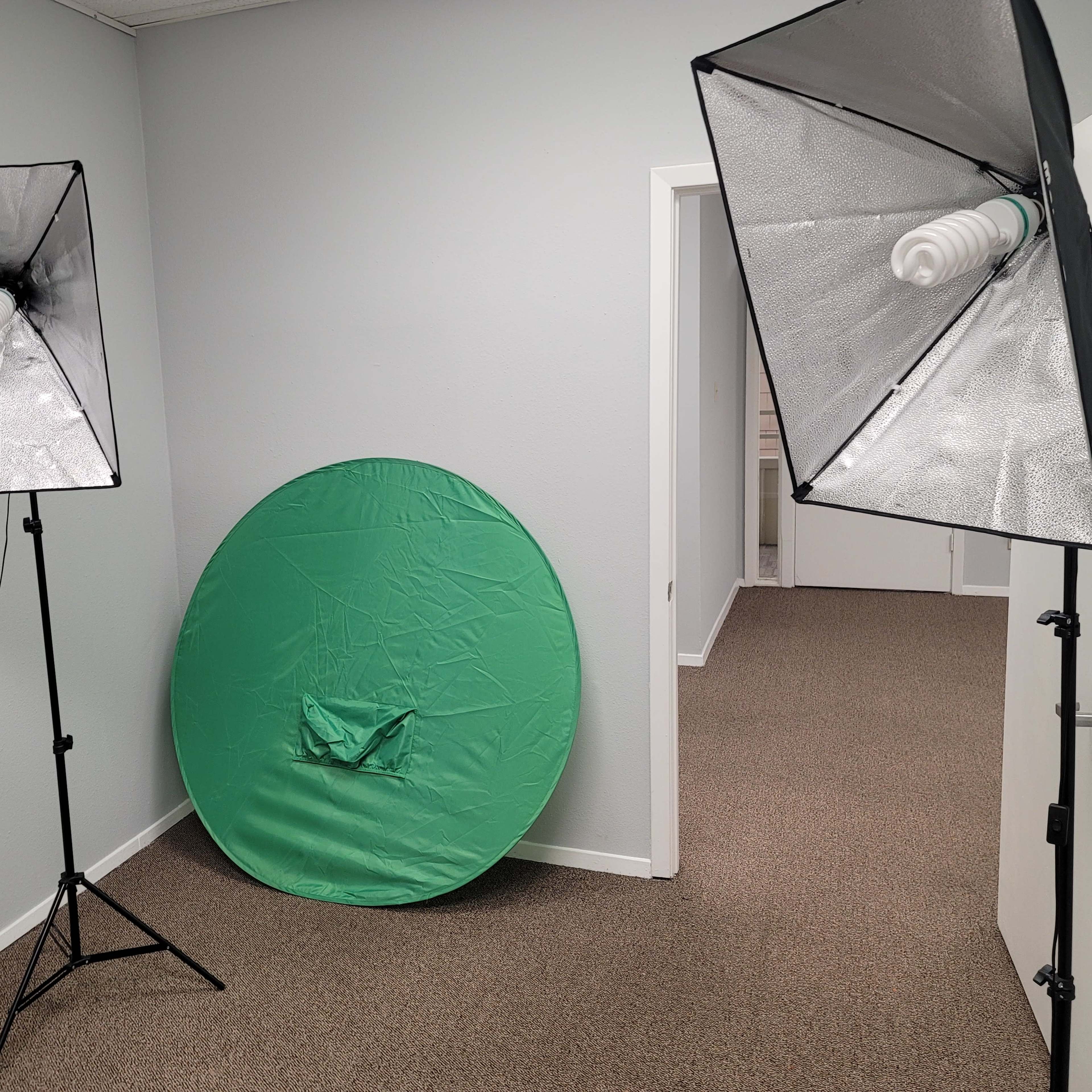 A room with two photography lights on stands and a collapsible green backdrop positioned on the floor.