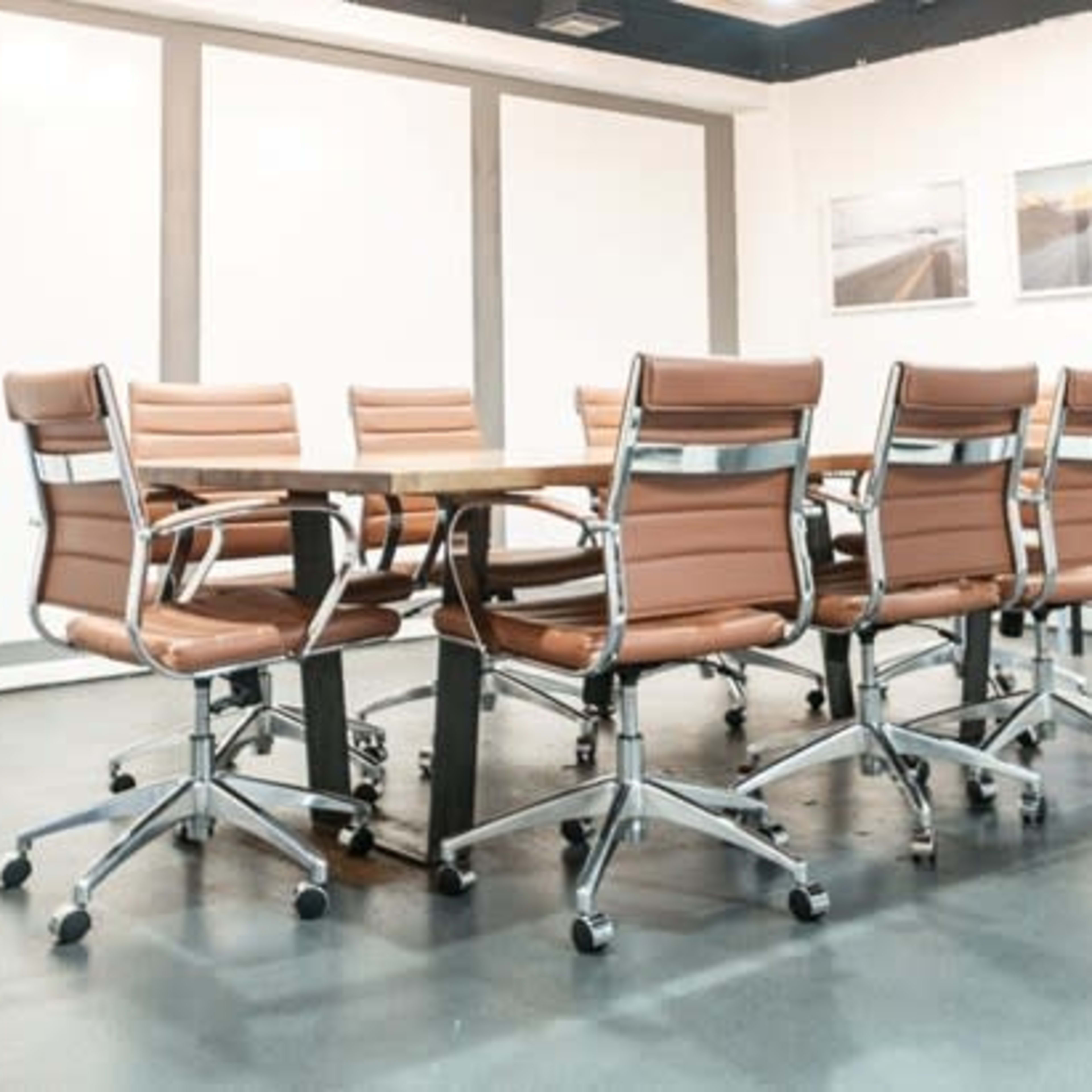 A modern conference room features a large table surrounded by ergonomic chairs with brown leather upholstery.